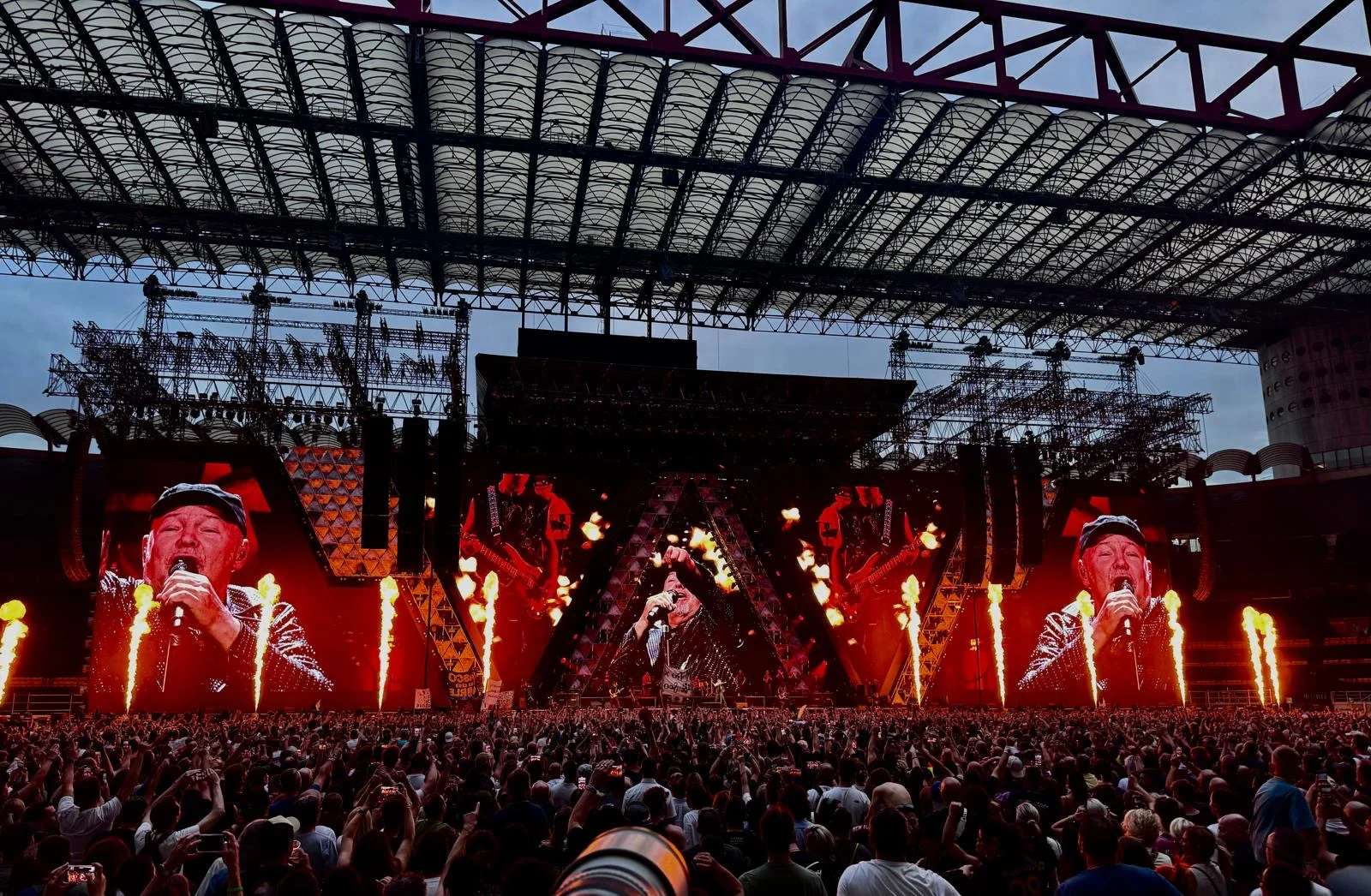 Getti di fiamme lungo il fronte del palco mentre gli schermi laterali mostrano il cantante, sotto la copertura dello stadio – Vasco Rossi Live 2024, Italia – scenografia per concerti