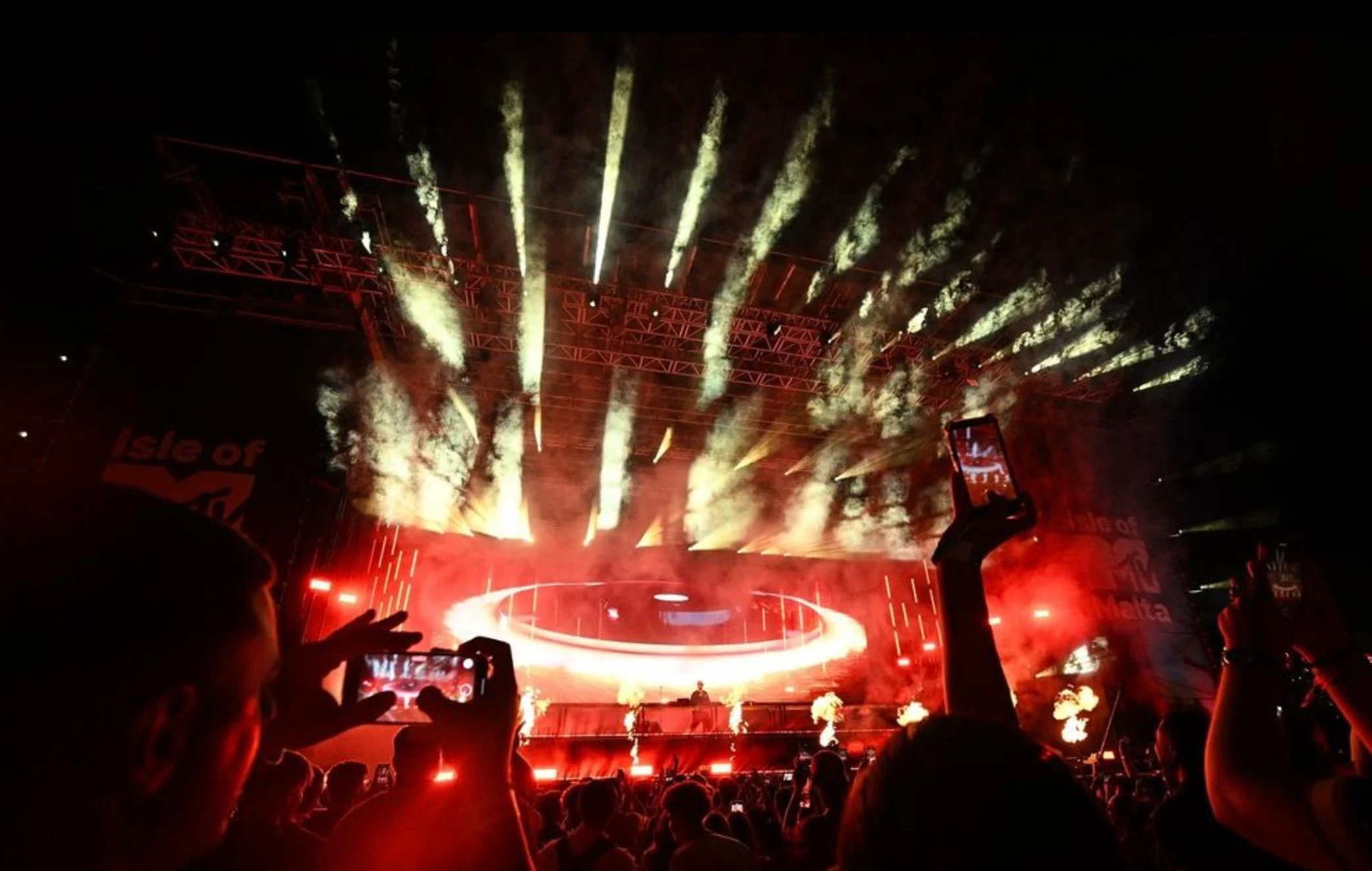 Palco illuminato di rosso con un anello circolare luminoso e fontane pirotecniche, fan che filmano con i telefoni – Isle of MTV 2024, Floriana, Malta – scenografia per concerti