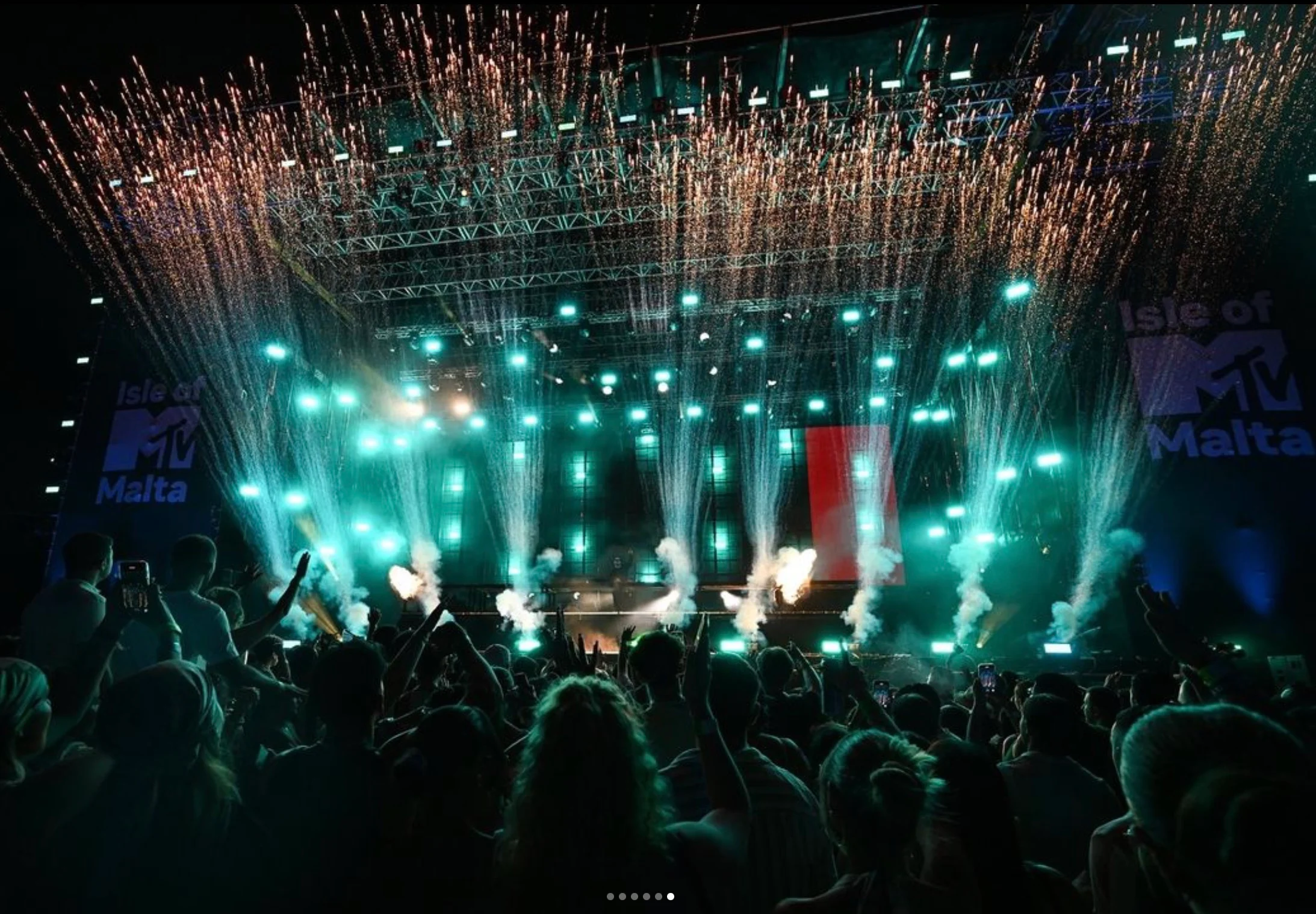 Palco di Isle of MTV Malta di notte: luci verde acqua e cascate di scintille su una folla con le mani alzate – Isle of MTV 2024, Floriana, Malta – scenografia per concerti