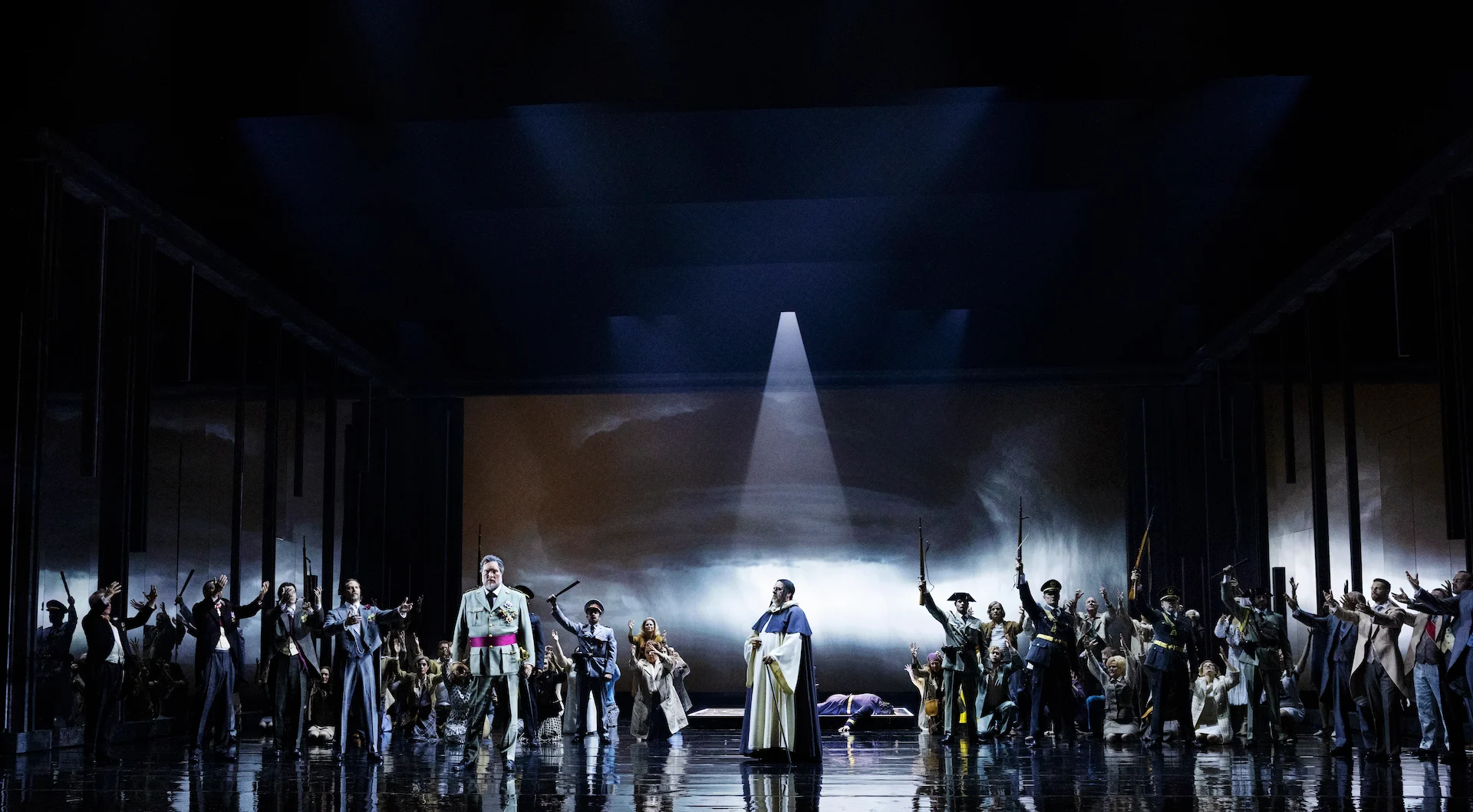 Artisti in uniforme con fucili alzati ai lati di un religioso, un fascio di luce su un fondale proiettato di nuvole – Don Carlo al Teatro Reale Danese, Copenaghen, Danimarca, 2024 – scenografia d'opera