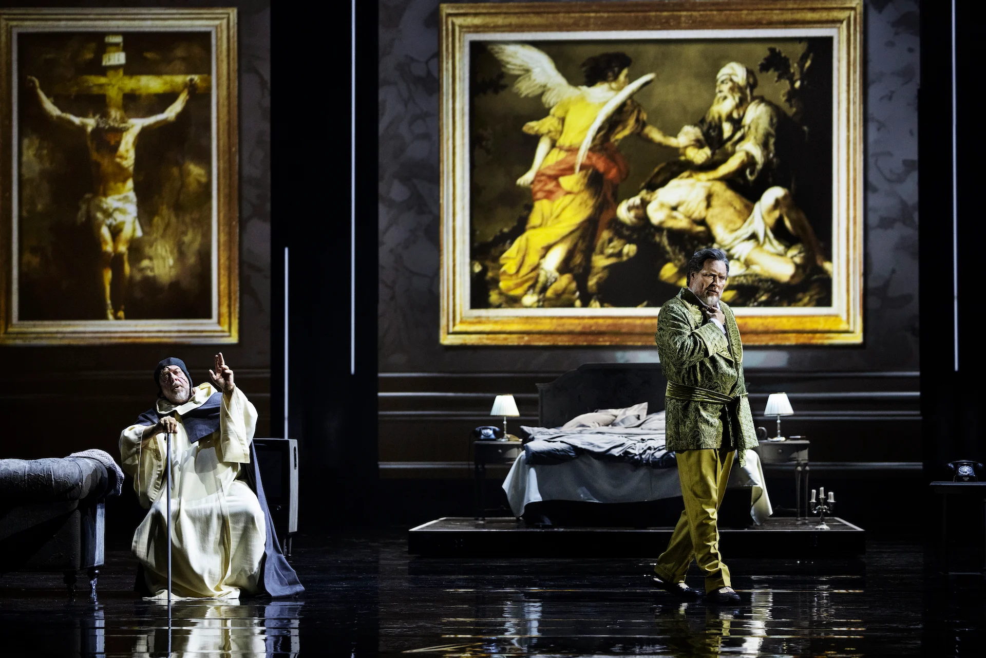 Scena in camera da letto con un religioso in bianco e un cantante in veste verde, dipinti religiosi incorniciati dietro – Don Carlo al Teatro Reale Danese, Copenaghen, Danimarca, 2024 – scenografia d'opera