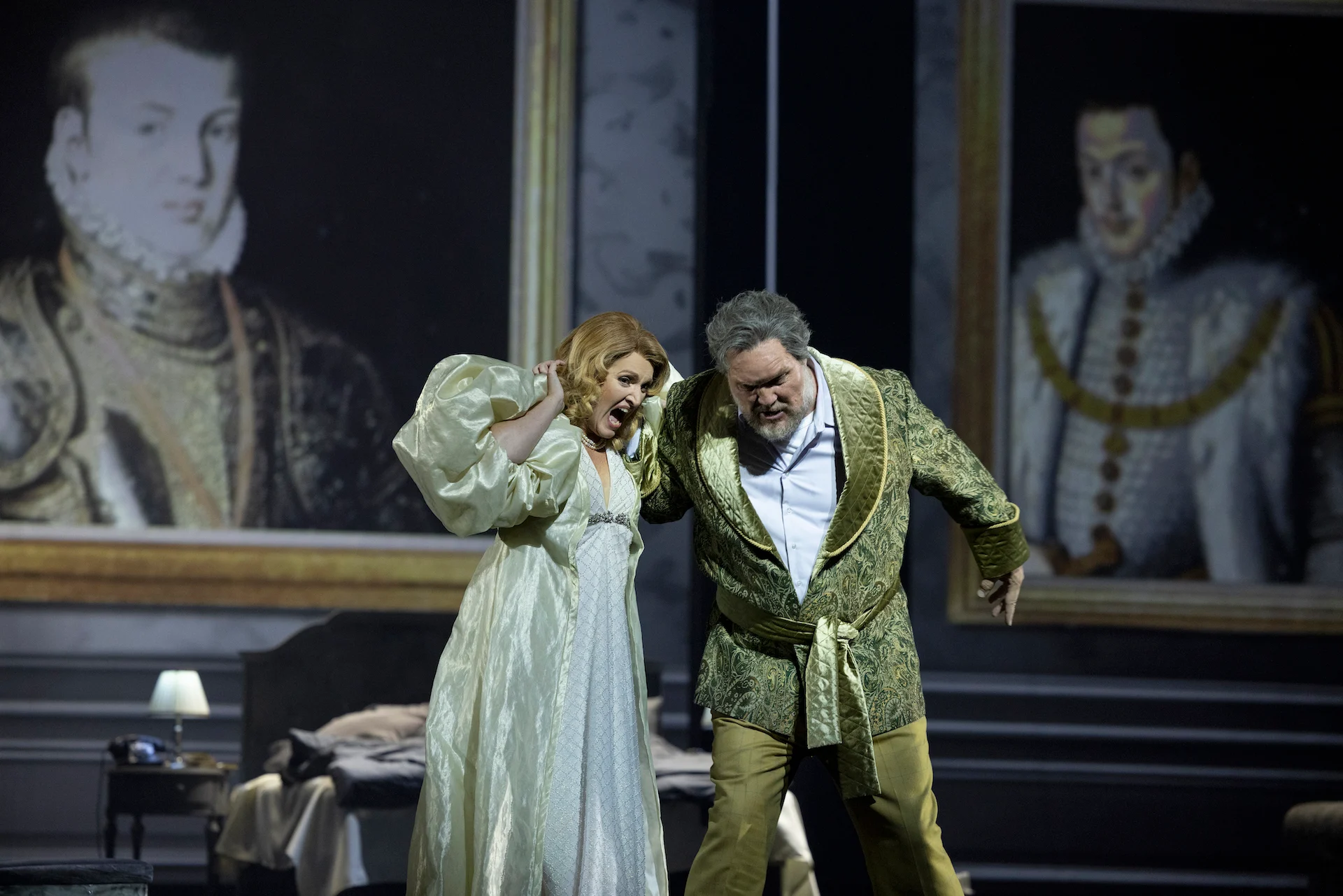Cantante in camicia da notte chiara che si ritrae da un uomo in veste verde, ritratti rinascimentali incorniciati dietro – Don Carlo al Teatro Reale Danese, Copenaghen, Danimarca, 2024 – scenografia d'opera