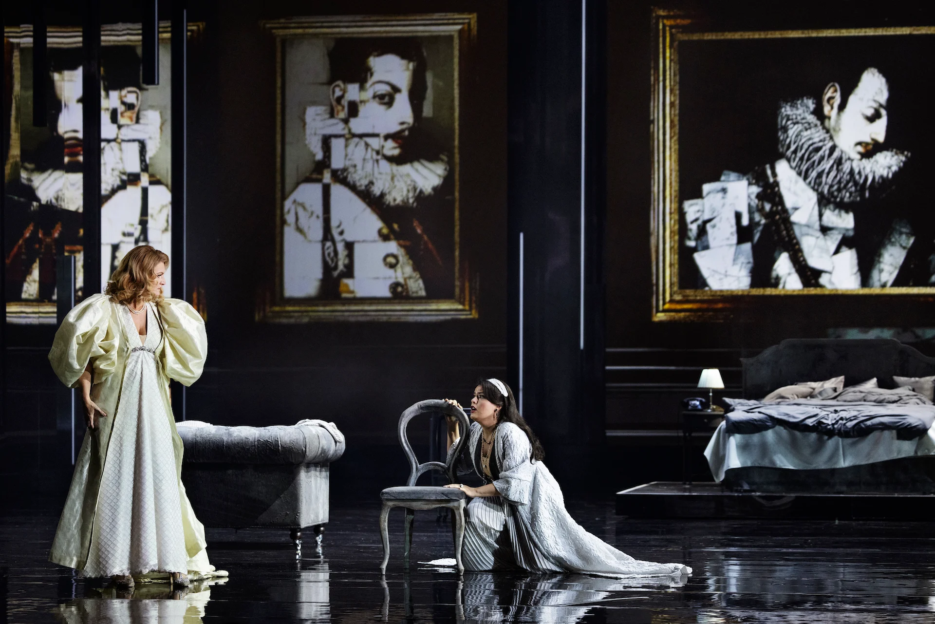 Donna in abito avorio di fronte a una donna inginocchiata accanto a una sedia, ritratti frammentati in cornici dorate – Don Carlo al Teatro Reale Danese, Copenaghen, Danimarca, 2024 – scenografia d'opera