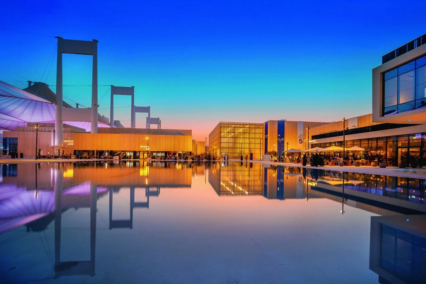 Sito della Biennale al tramonto sotto un cielo blu e arancione, padiglioni e piloni delle tende riflessi in una lunga vasca – Biennale delle Arti Islamiche, Jeddah, Arabia Saudita, 2023 – architettura