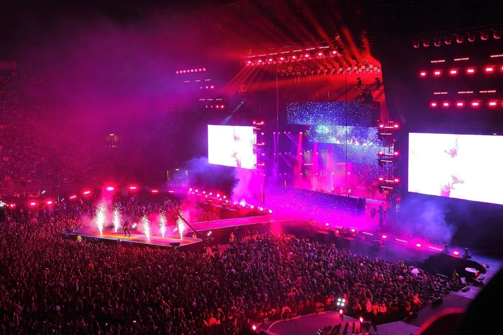 Pubblico dello stadio in luce magenta, fontane di scintille su una passerella e grandi schermi laterali – Cesare Cremonini Stadi 2018, Italia – scenografia per concerti