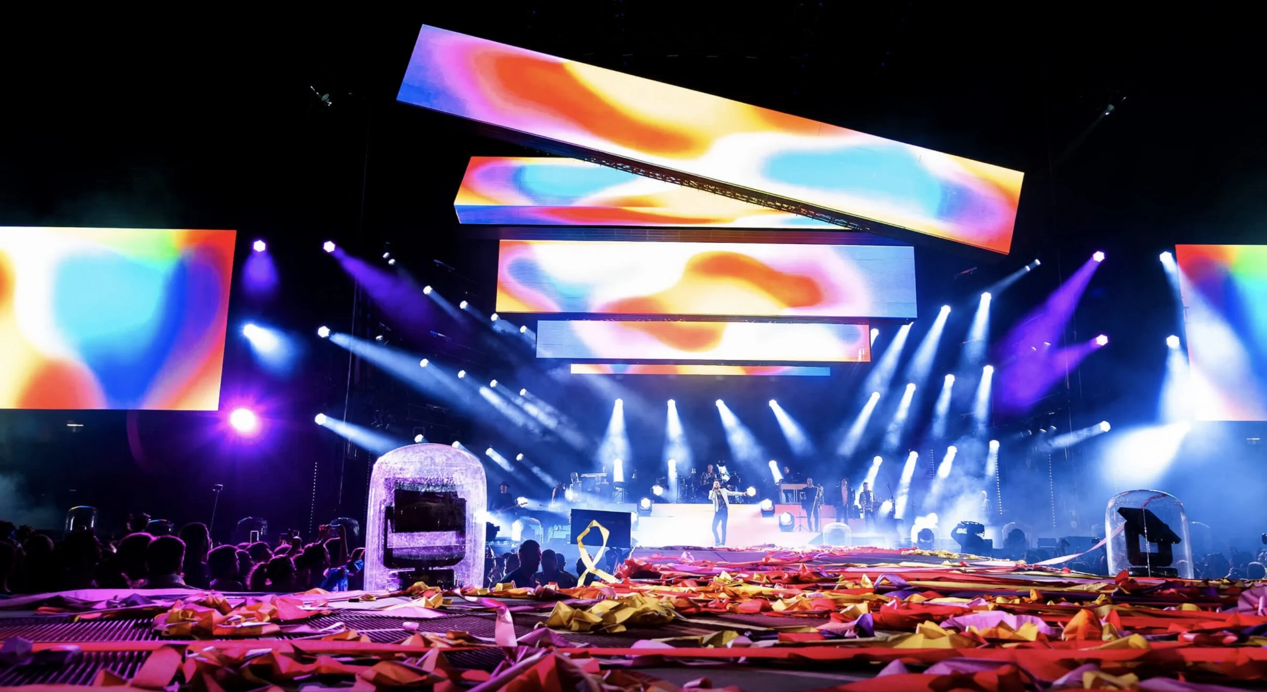Vista d'insieme del palco negli stadi di Cremonini: barre video inclinate in colori vivaci sopra fasci di luce – Cesare Cremonini Stadi 2018, Italia – scenografia per concerti