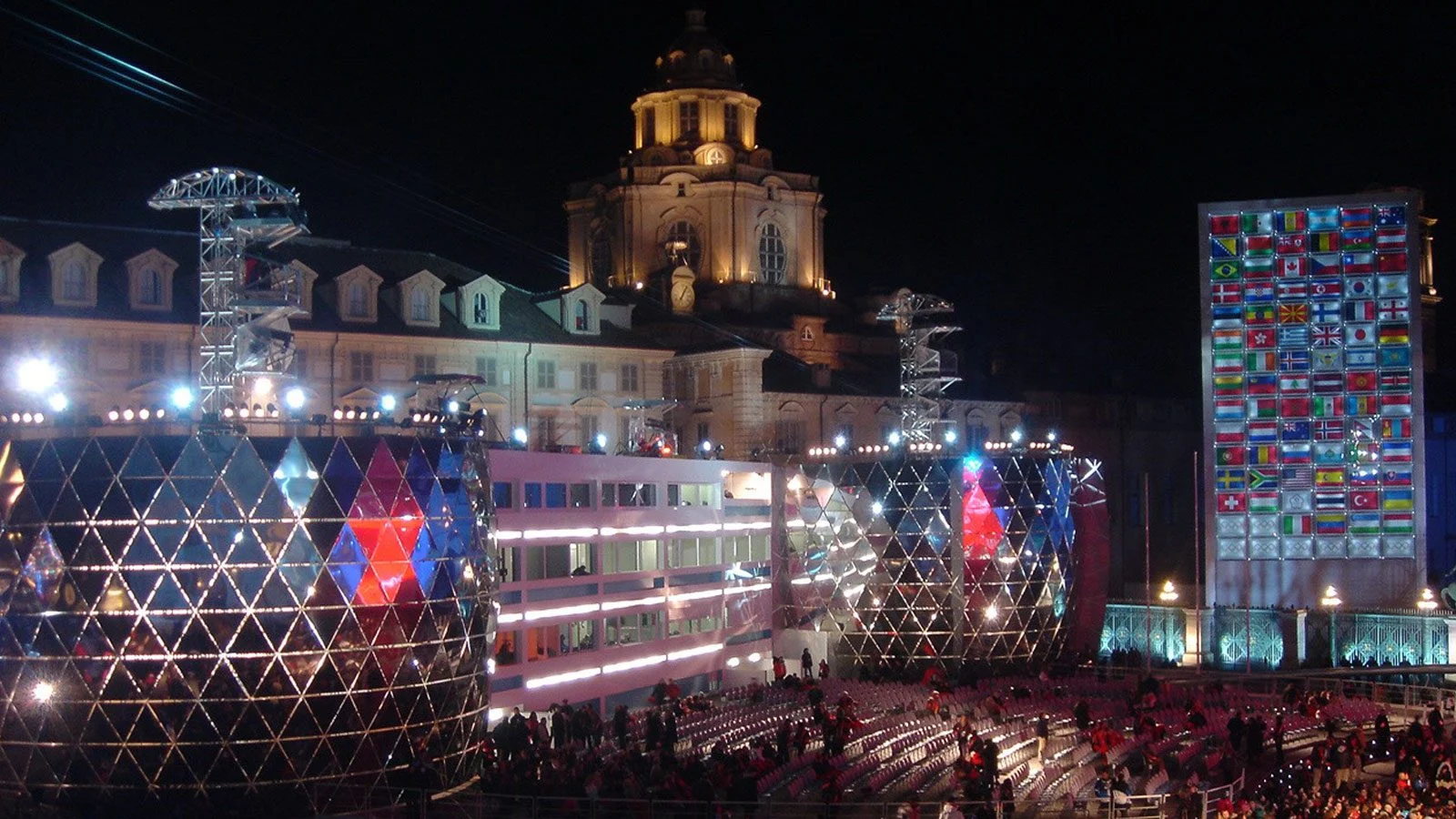 Vista notturna di Piazza Castello con padiglioni luminosi geodetici, una parete di bandiere e la chiesa con cupola dietro – Medals Plaza, Olimpiadi invernali di Torino 2006, Italia – progettazione di eventi