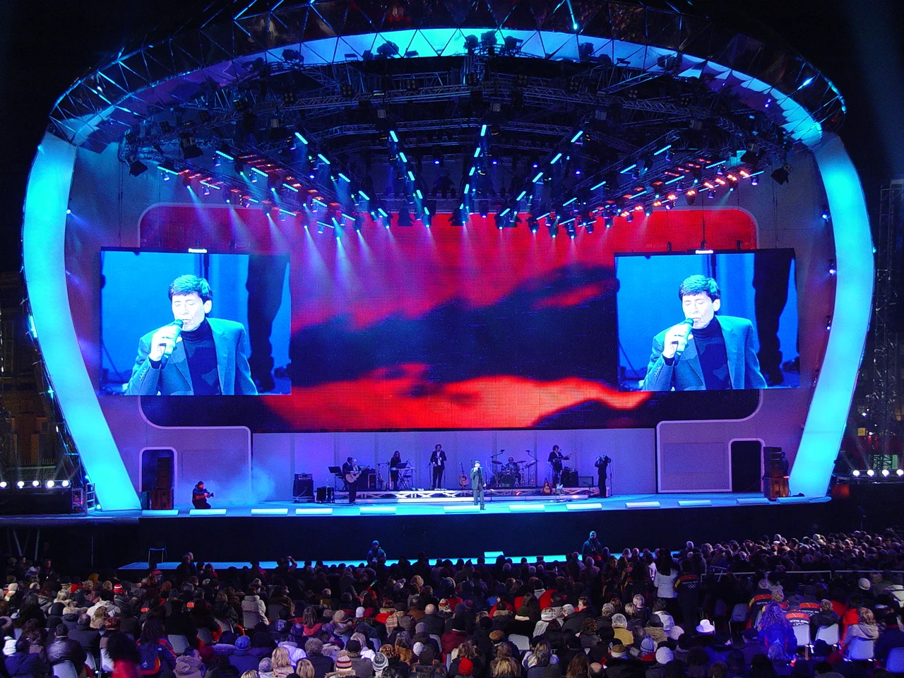 Concerto sul palco della Medals Plaza: cantante sugli schermi laterali, grafiche di cielo rosso e band sotto l'impianto luci – Medals Plaza, Olimpiadi invernali di Torino 2006, Italia – progettazione di eventi