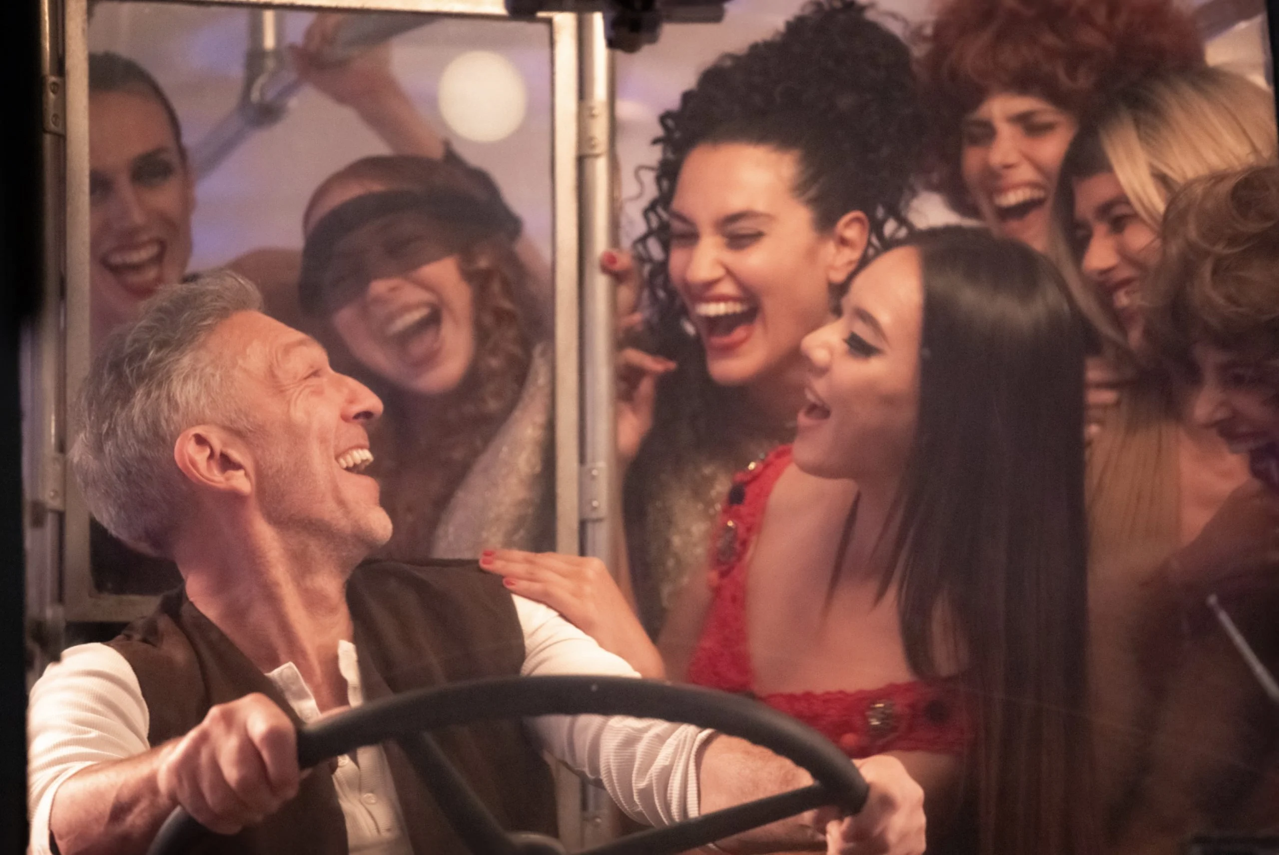 Fotogramma del film: artisti che ridono stretti intorno a un autista al volante di un autobus – The Opera! Arie per un'Eclissi alla Festa del Cinema di Roma, Italia, 2024 – scenografia