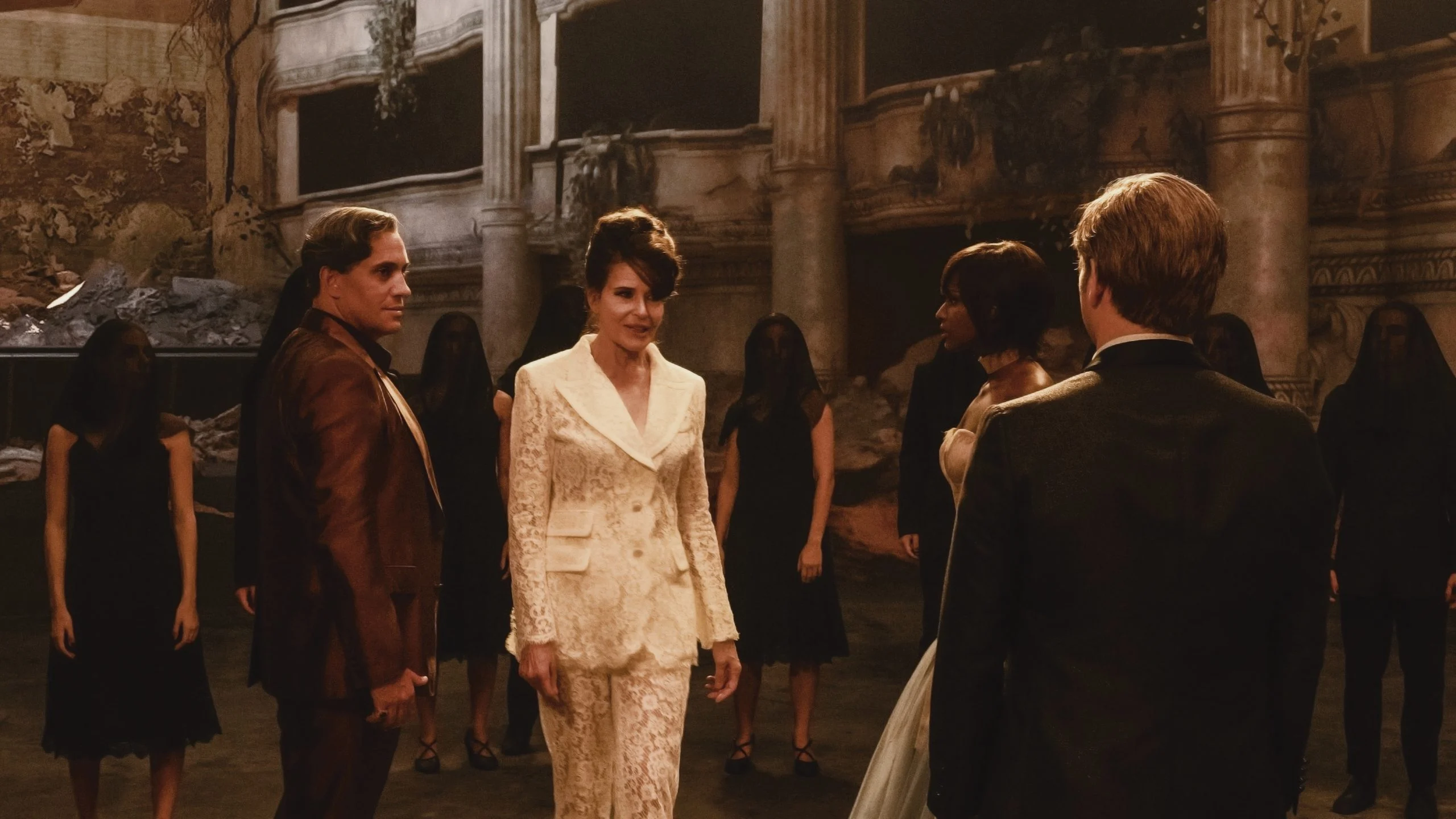 Fotogramma del film: una donna in tailleur di pizzo bianco tra figure in nero in un teatro in rovina – The Opera! Arie per un'Eclissi alla Festa del Cinema di Roma, Italia, 2024 – scenografia