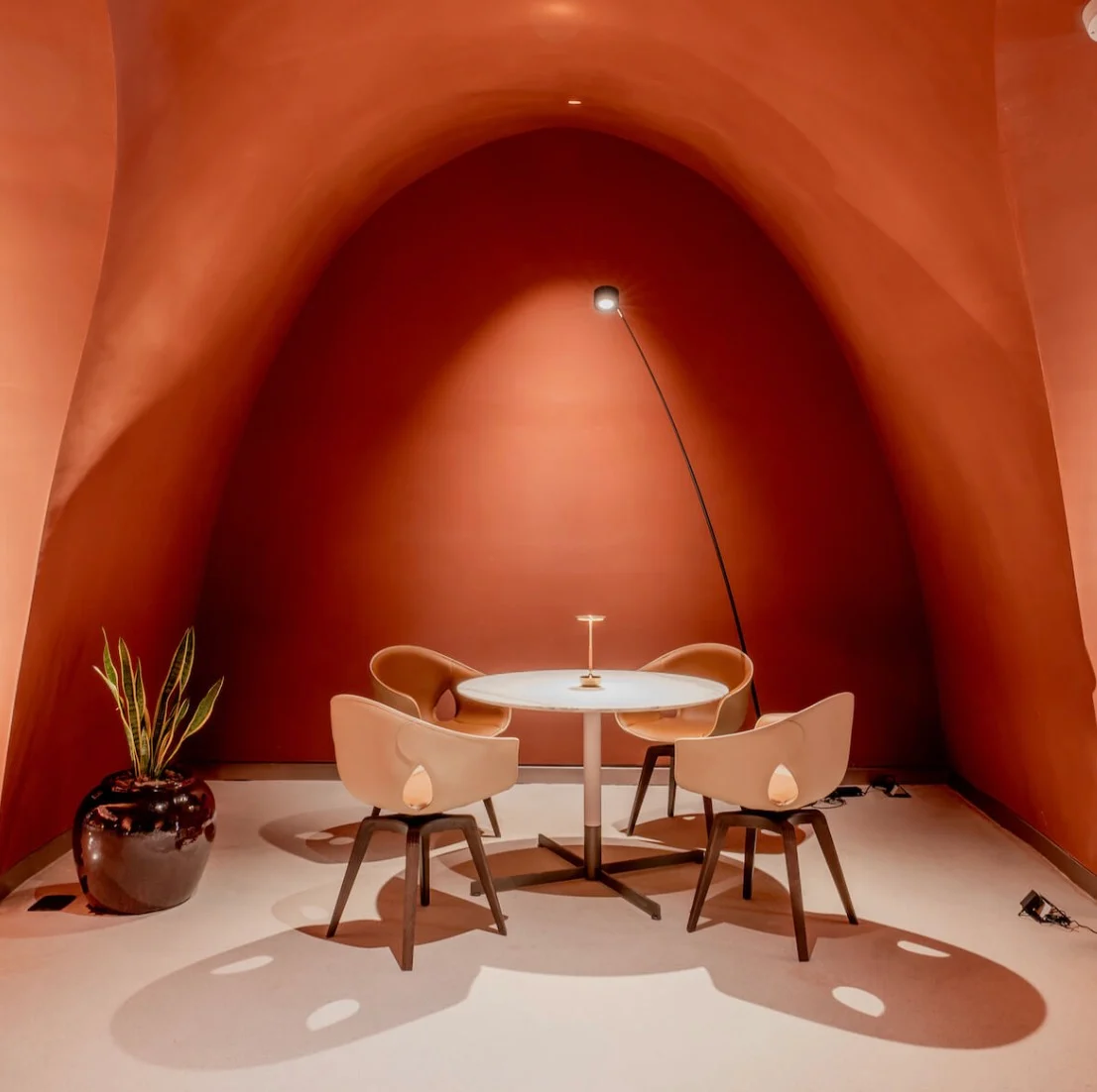 Quattro sedie in pelle intorno a un tavolo rotondo in un'alcova in terracotta illuminata da una lampada ad arco – King Fahad Chair per Poltrona Frau, Riyadh, Arabia Saudita, 2024 – design di prodotto