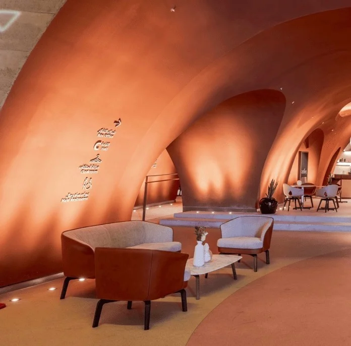 Poltrone e divano in pelle in una lounge voltata in terracotta, con segnaletica a parete e un caffè oltre – King Fahad Chair per Poltrona Frau, Riyadh, Arabia Saudita, 2024 – design di prodotto