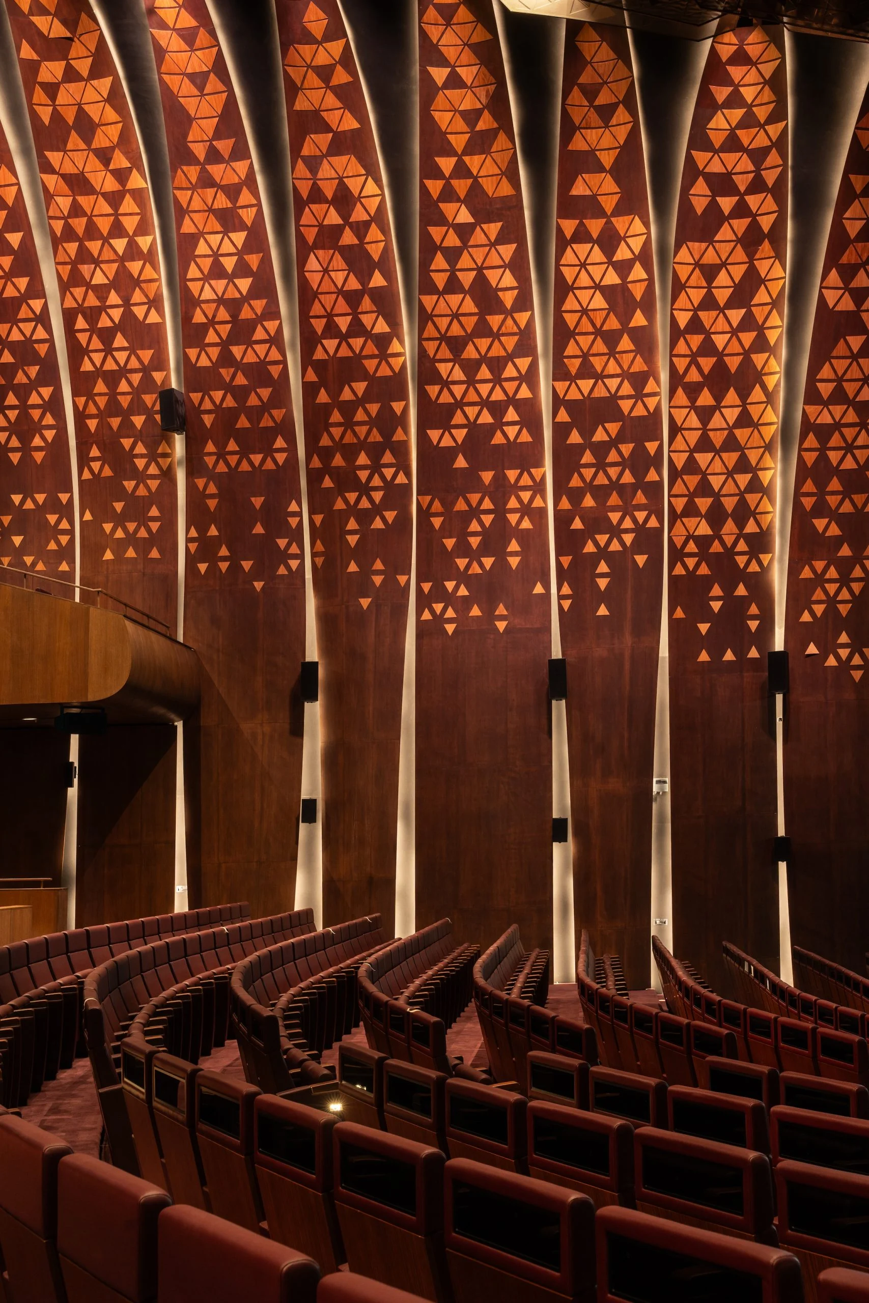 File di poltrone King Fahad nella sala sotto pannelli a parete con un motivo triangolare in legno – King Fahad Chair per Poltrona Frau, Riyadh, Arabia Saudita, 2024 – design di prodotto
