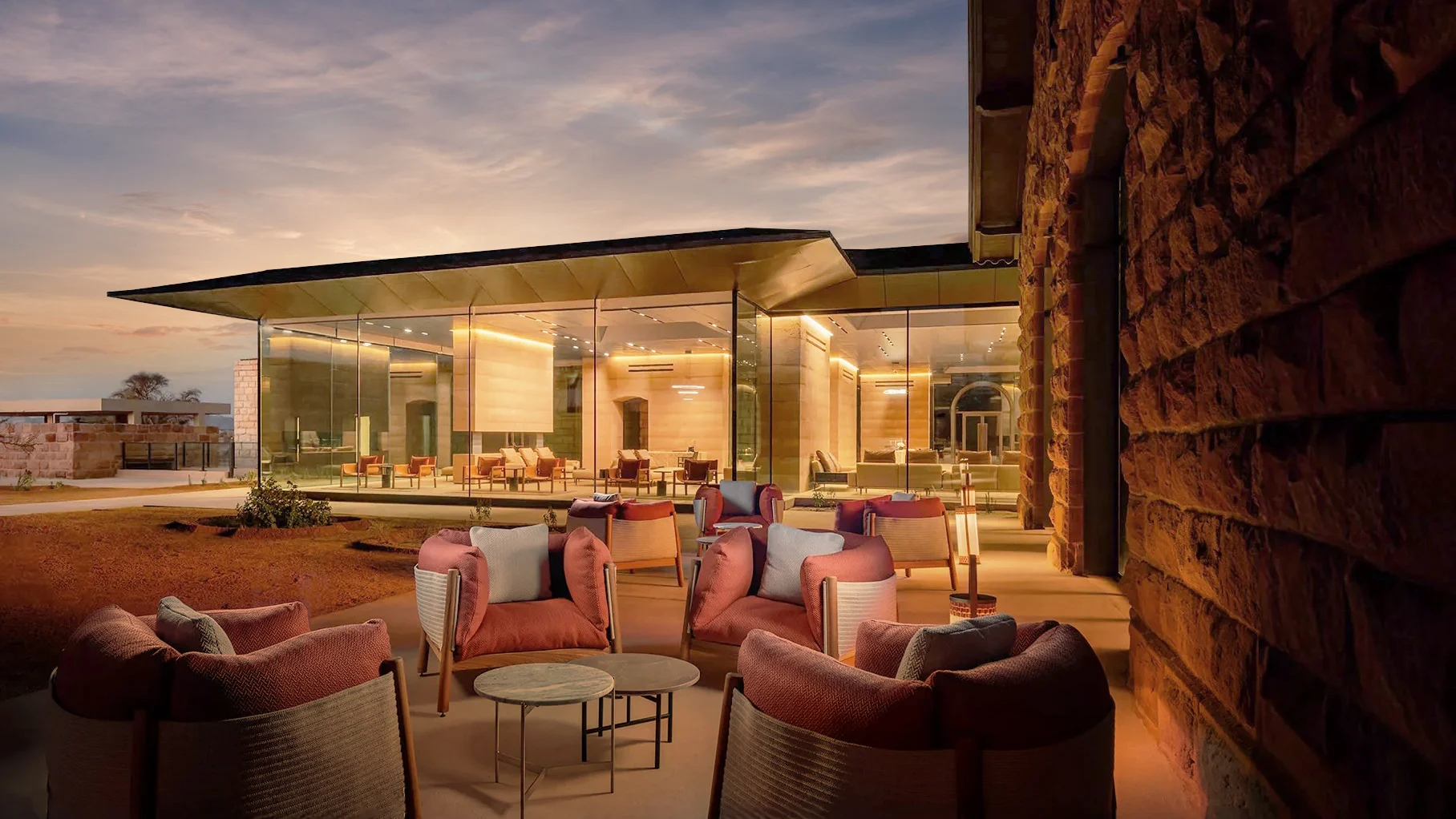 Terrazza con poltrone rosa al tramonto davanti a un padiglione in vetro e a un muro in pietra grezza – The Chedi Hegra, AlUla, Arabia Saudita, 2024 – architettura alberghiera
