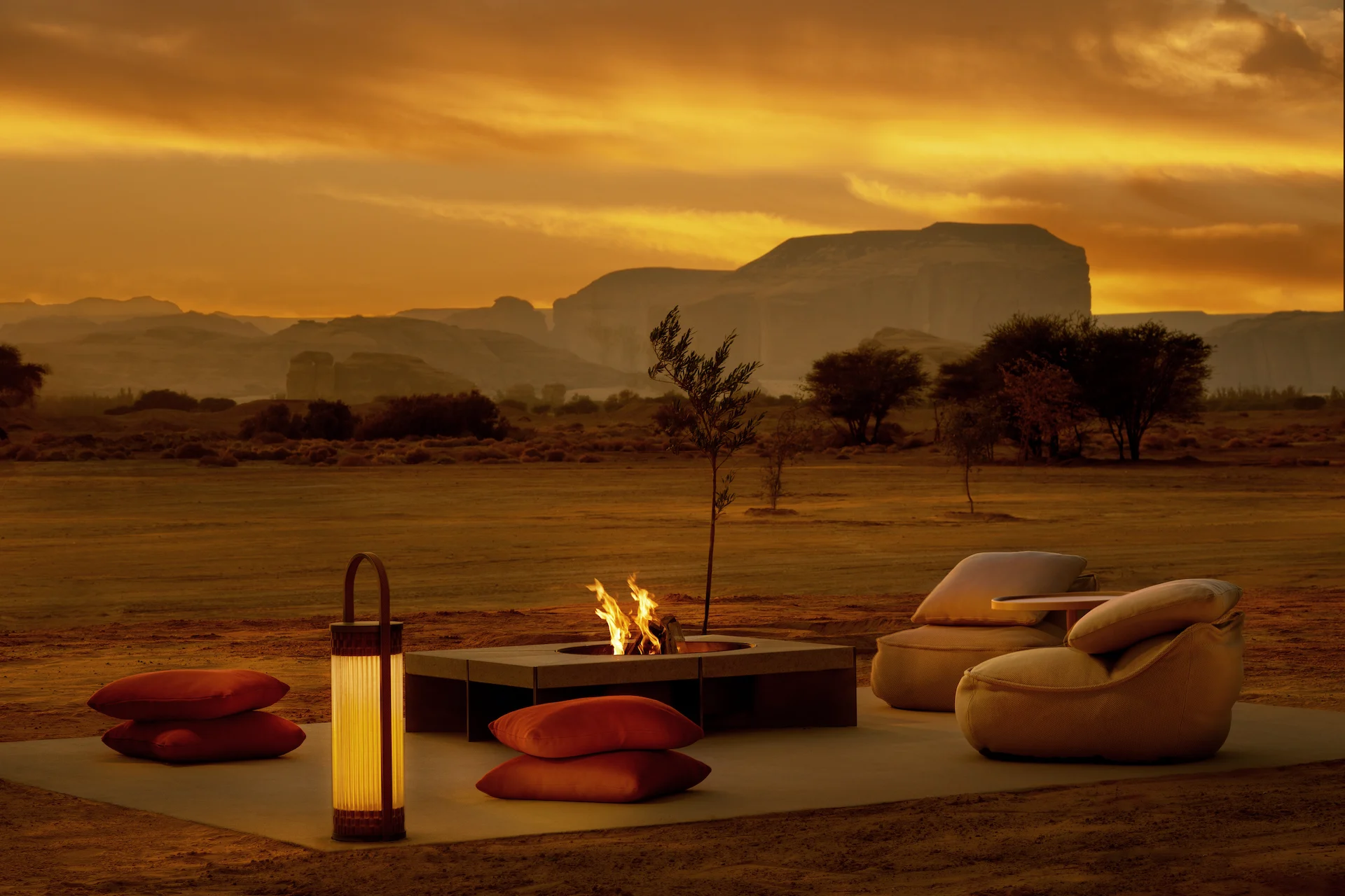 Braciere all'aperto con cuscini a terra, lanterna e sedute lounge nel deserto sotto un cielo arancione al tramonto – The Chedi Hegra, AlUla, Arabia Saudita, 2024 – architettura alberghiera