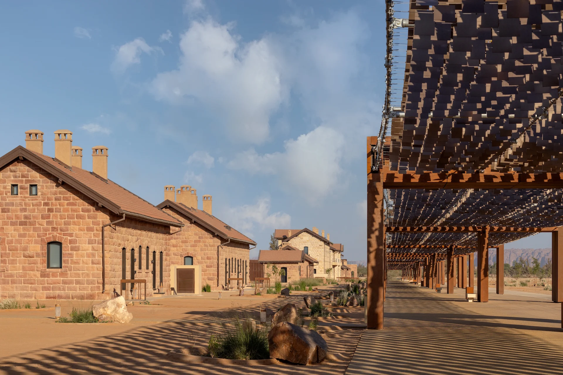 Fila di edifici in pietra restaurati della stazione accanto a una pergola in legno che proietta ombre a strisce – The Chedi Hegra, AlUla, Arabia Saudita, 2024 – architettura alberghiera