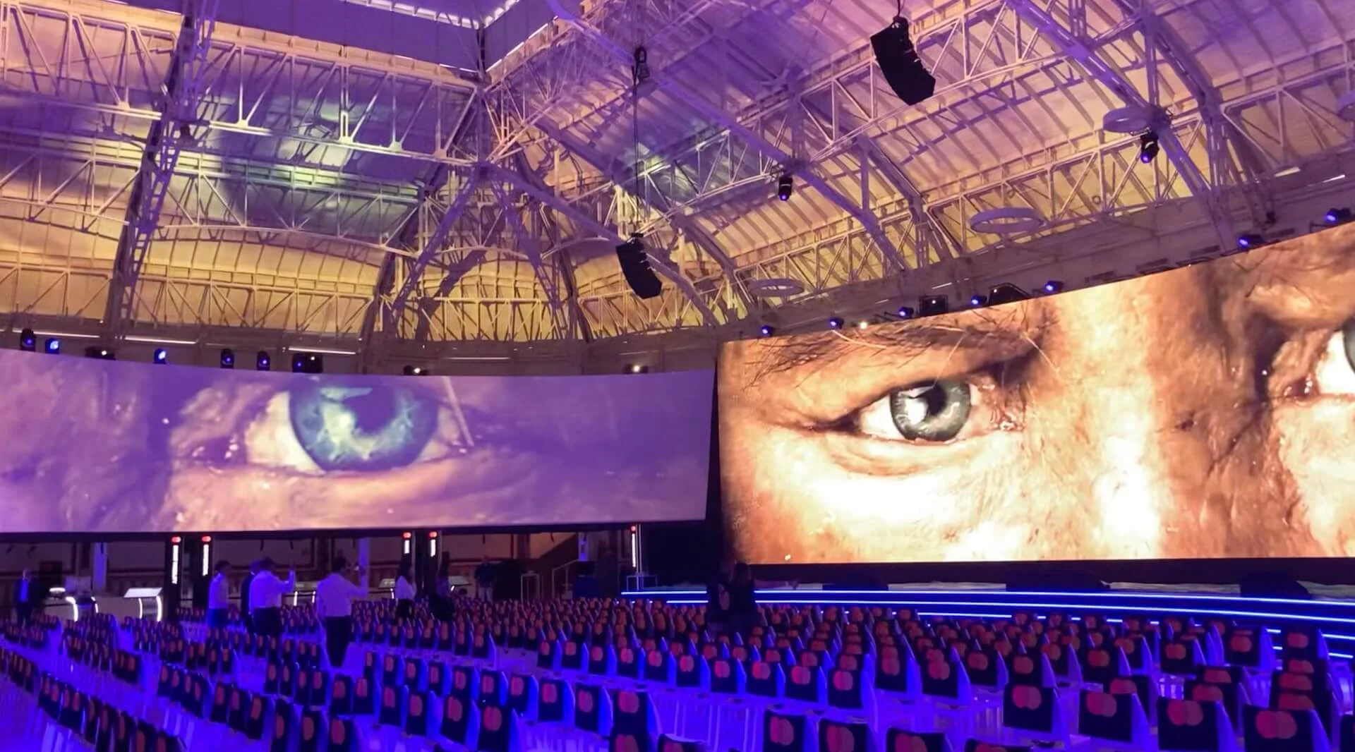 Sala del Mastercard Innovation Forum: schermi LED curvi con occhi giganti sopra file di sedie, luce viola – Mastercard Innovation Forum 2024, Milano, Italia – progettazione di eventi