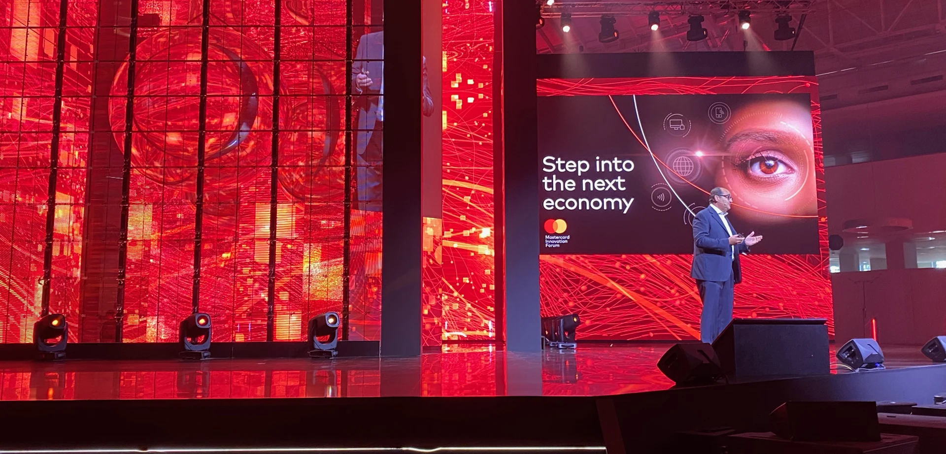 Relatore sul palco del Mastercard Innovation Forum tra pareti LED rosse e uno schermo con la scritta Step into the next economy – Mastercard Innovation Forum 2023, Milano, Italia – progettazione di eventi