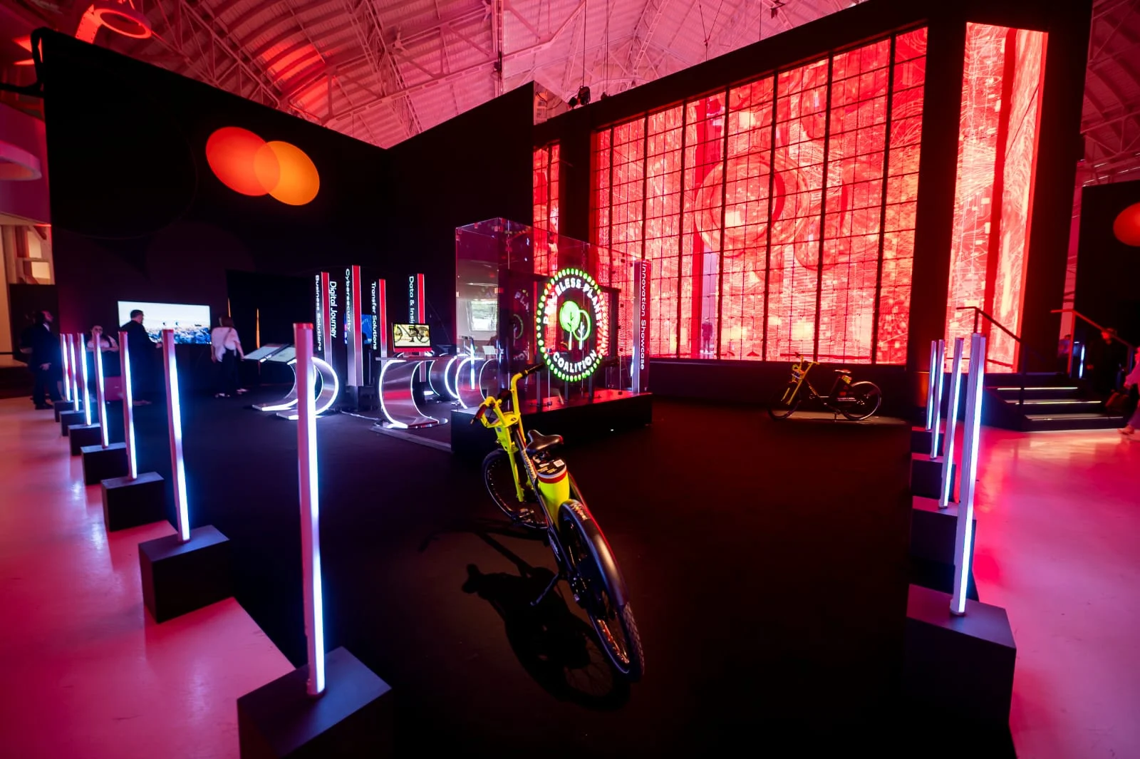 Demo Area del Mastercard Innovation Forum: pali luminosi al neon, una e-bike gialla e un cubo di vetro sotto pareti LED rosse – Mastercard Innovation Forum 2023, Milano, Italia – progettazione di eventi