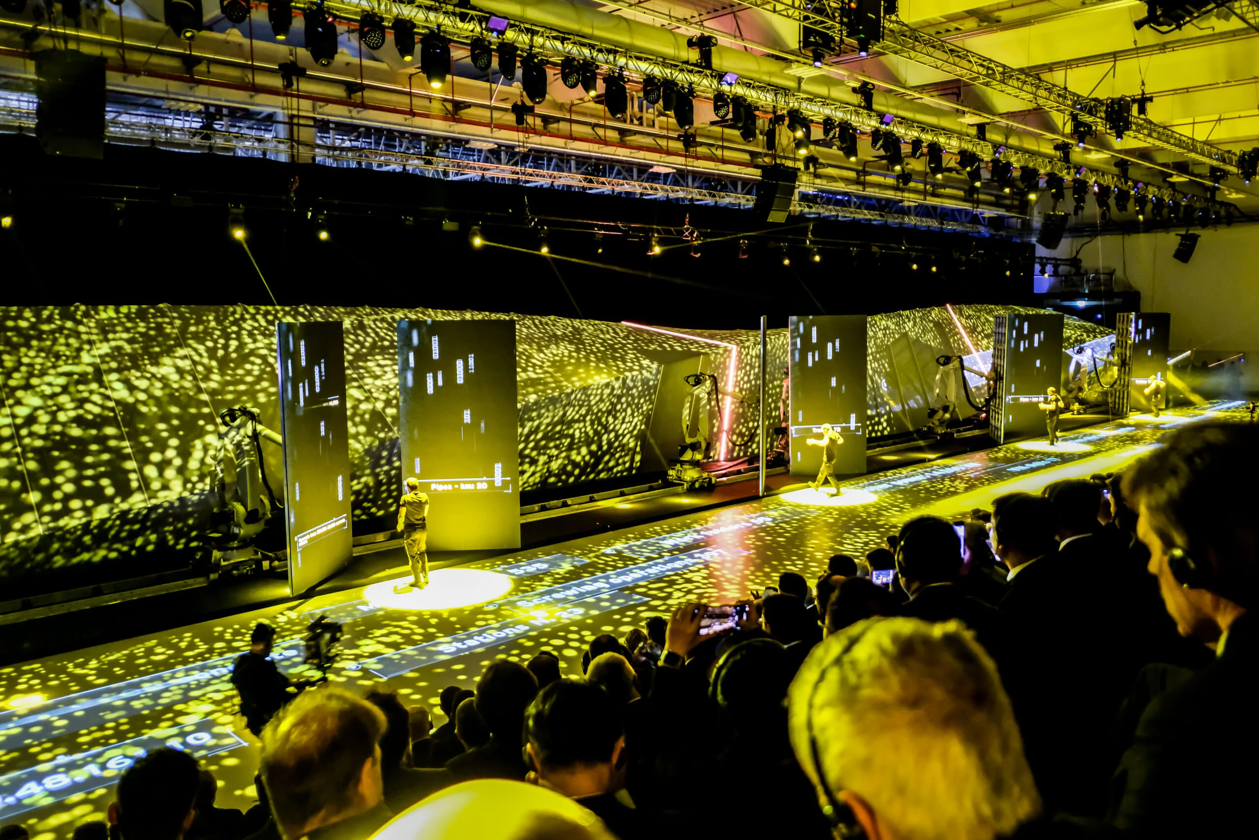 Pubblico che segue lo show lungo il palco, robot e schermi in un campo di luce gialla proiettata – Anteprima mondiale Lamborghini Urus, Sant'Agata Bolognese, Italia, 2017 – progettazione di eventi