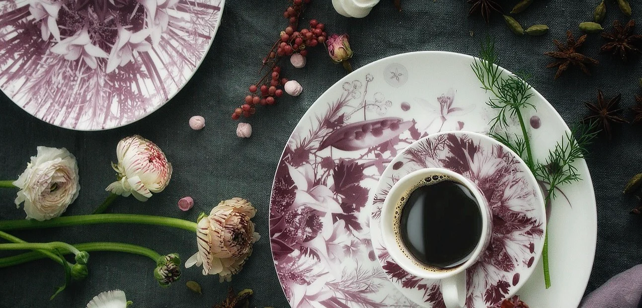 Tazza da caffè e piattino con decoro botanico prugna su un piatto decorato, con ranuncoli e bacche su tessuto scuro – Servizio da tavola Botanica per Bitossi Home, 2017 – design di prodotto