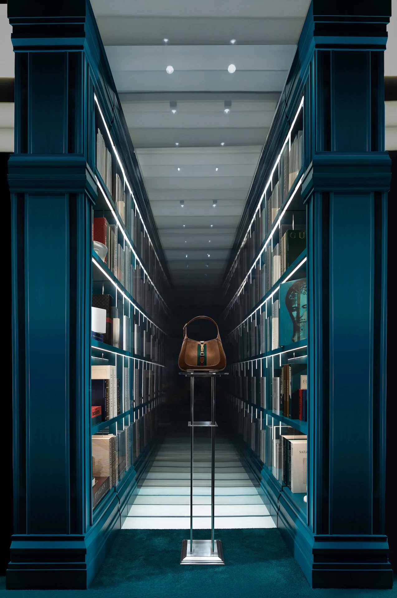 Corridoio a specchi di librerie verde-azzurro con una borsa Gucci su un supporto al centro – Vetrine Gucci Endless Narratives, 2025 – retail design