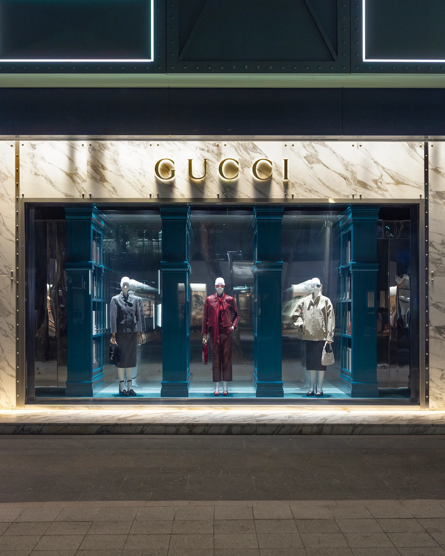 Vetrina Gucci in una facciata di marmo: tre manichini tra colonne verde-azzurro e librerie a specchio – Vetrine Gucci Endless Narratives, 2025 – retail design
