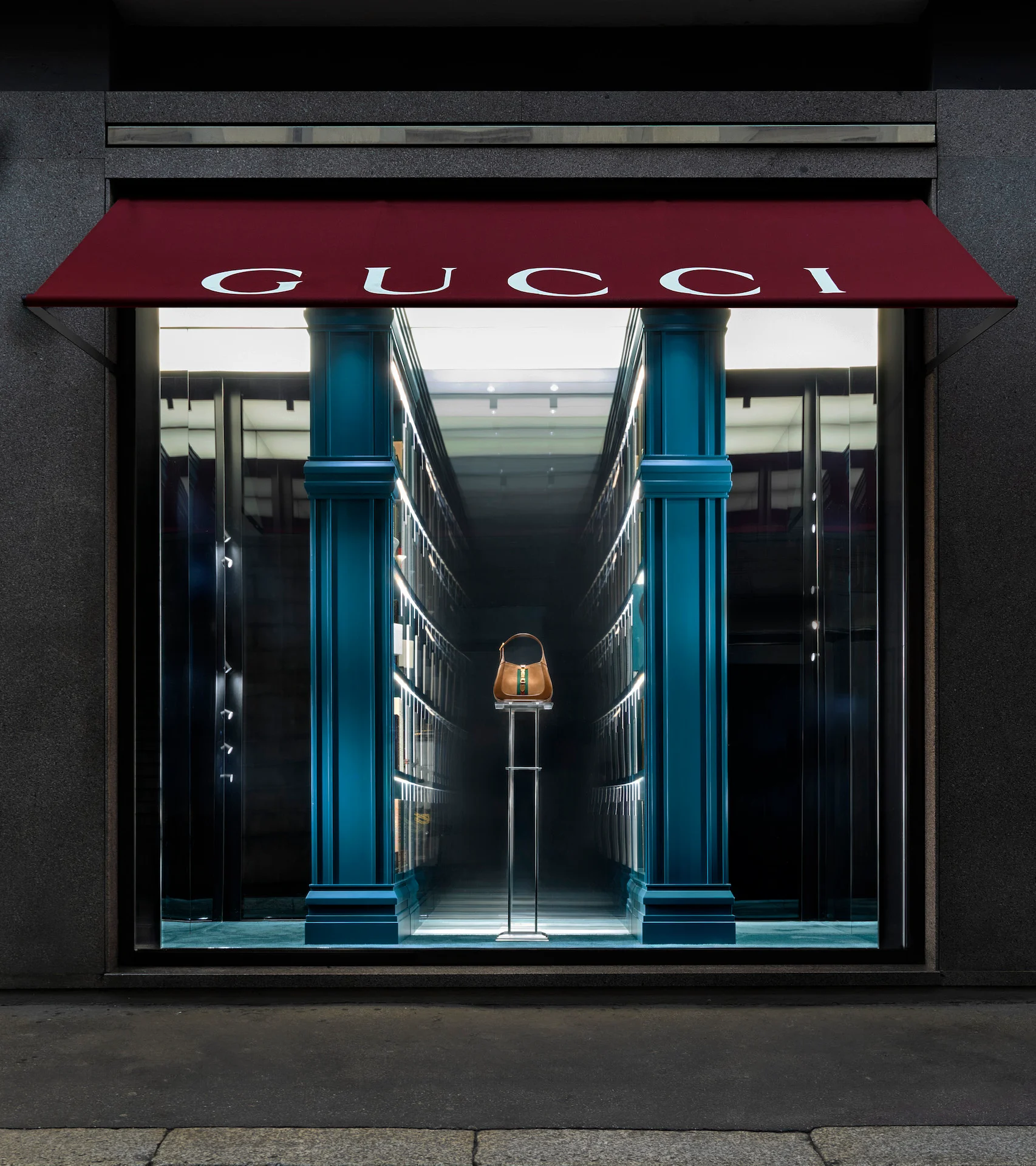 Vetrina Gucci sotto una tenda rossa: un'unica borsa in fondo a un corridoio infinito di librerie – Vetrine Gucci Endless Narratives, 2025 – retail design