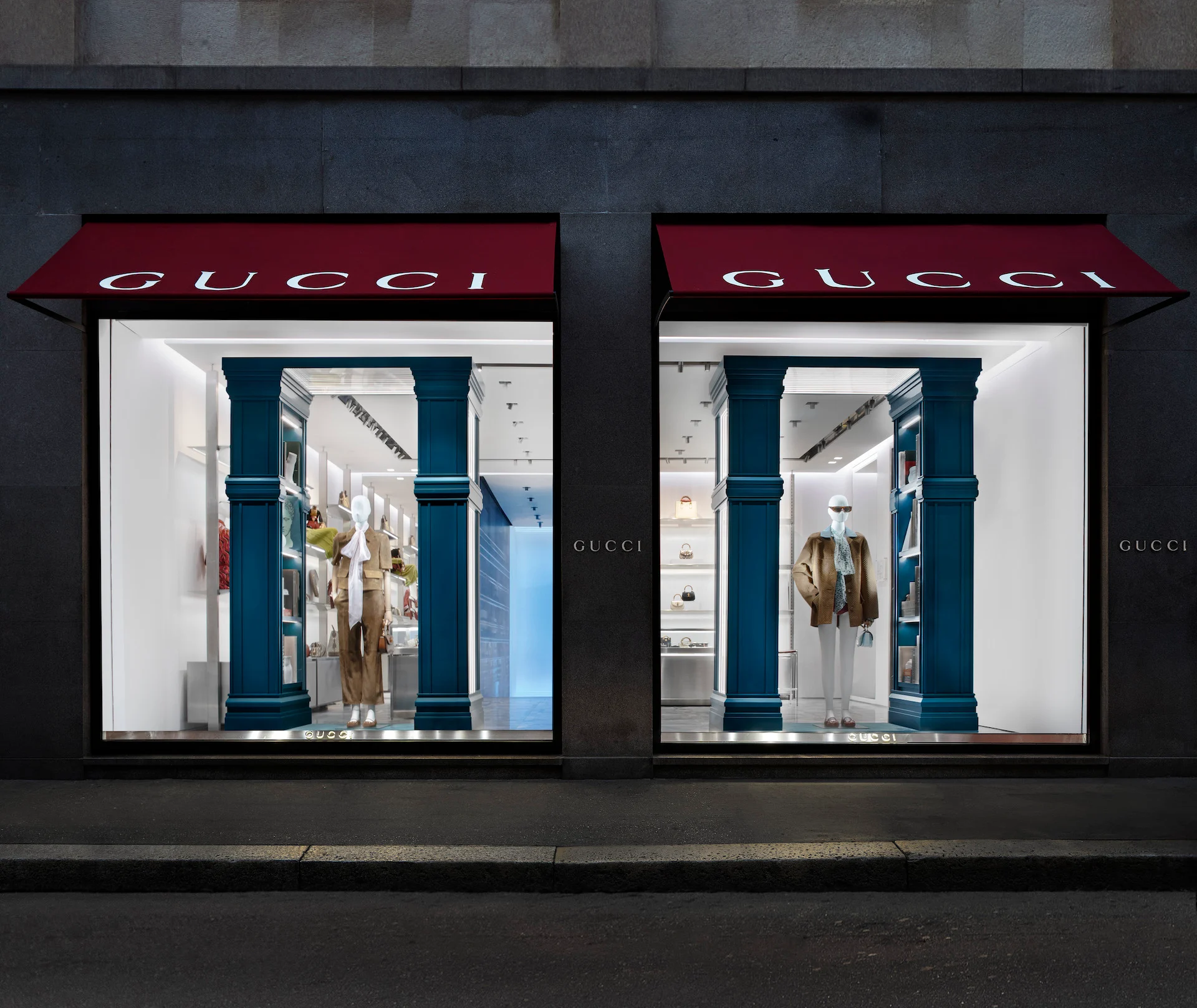 Due vetrine Gucci di notte sotto tende rosse, tra colonne verde-azzurro con manichini e scaffali illuminati – Vetrine Gucci Endless Narratives, 2025 – retail design
