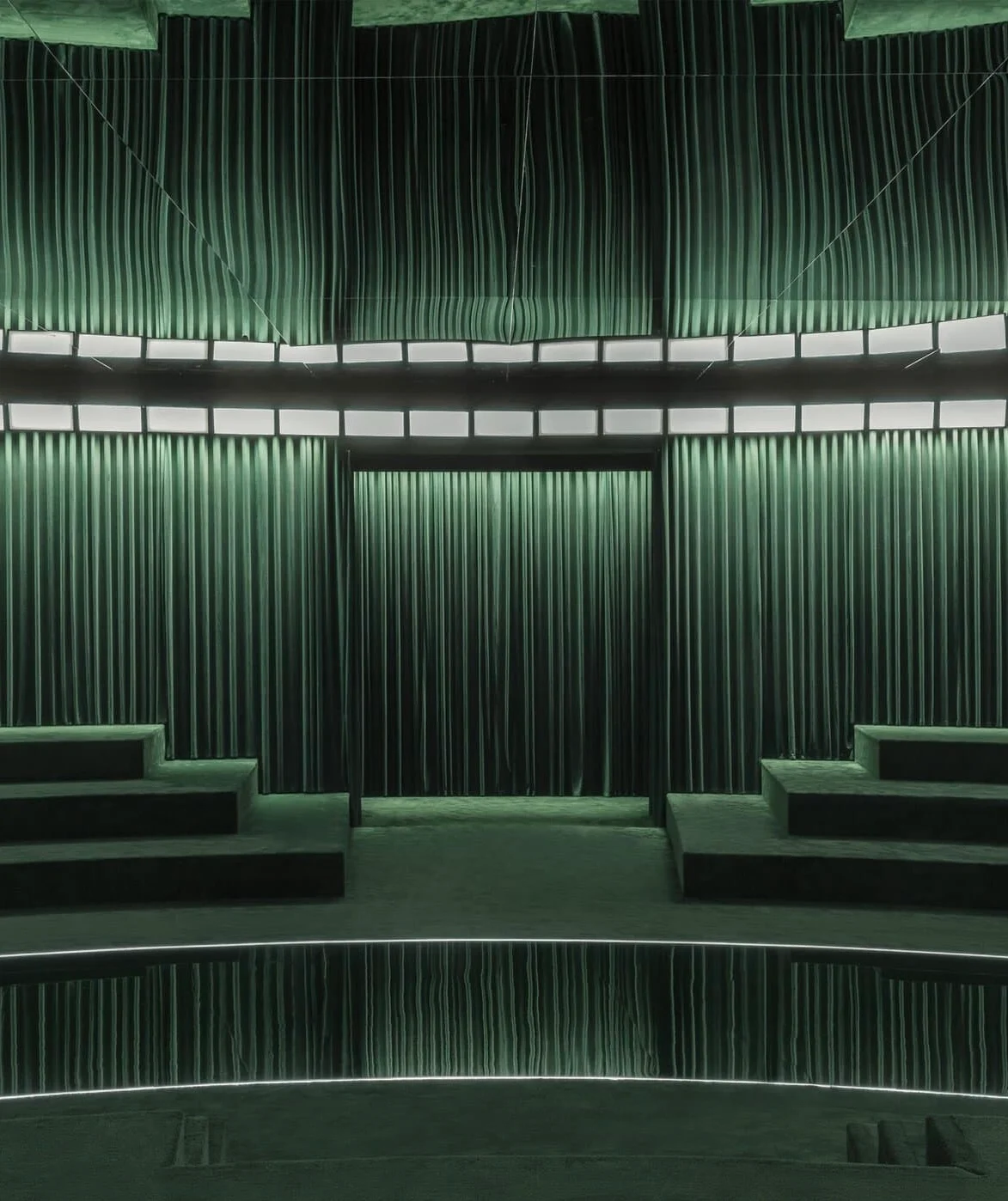 Vista frontale dell'ingresso della passerella con tende, tra gradinate in velluto verde – Gucci Autunno/Inverno 2025, Milano, Italia – scenografia per sfilate