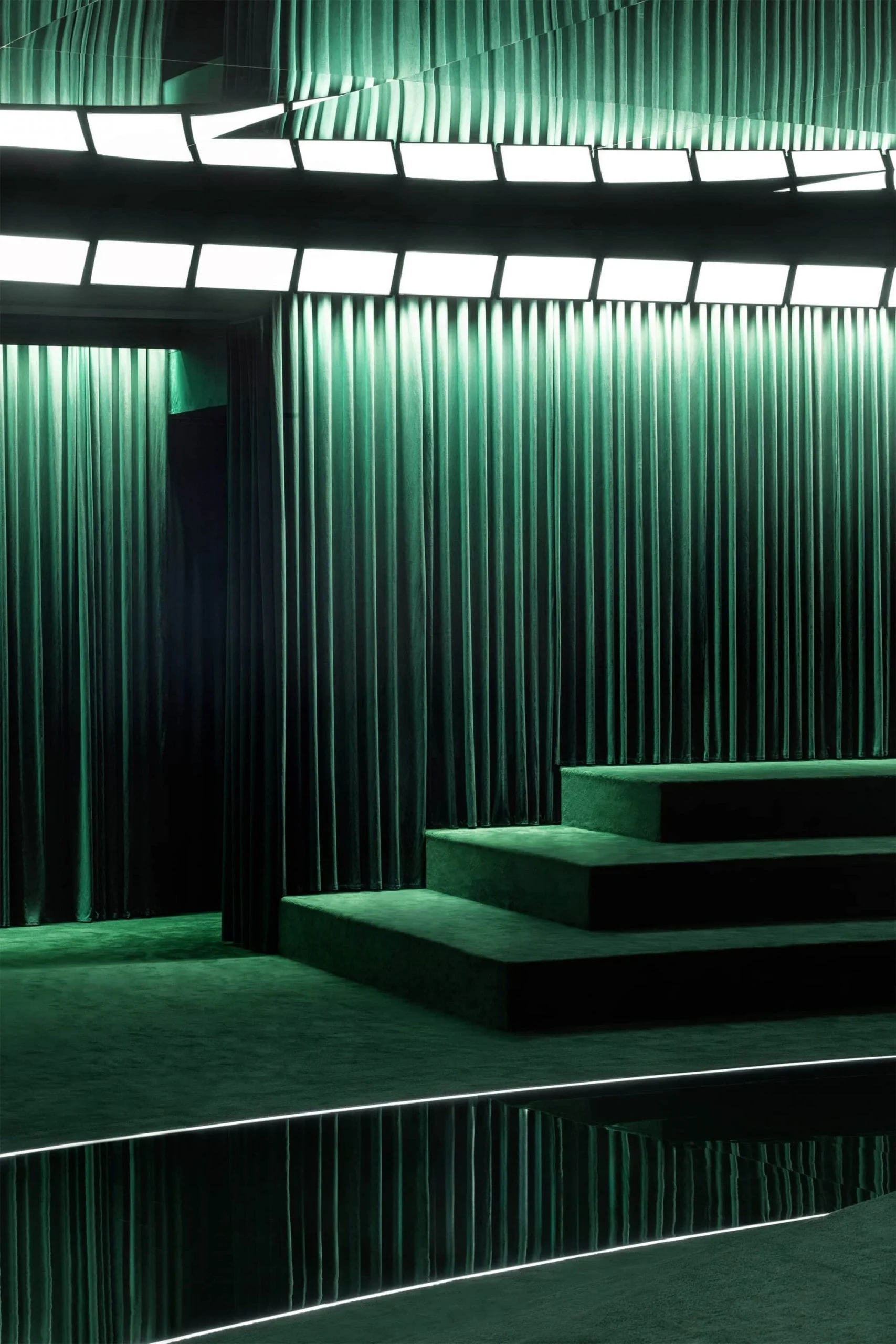 Dettaglio di gradini in velluto verde e tende plissettate illuminati da un anello di pannelli luminosi bianchi – Gucci Autunno/Inverno 2025, Milano, Italia – scenografia per sfilate