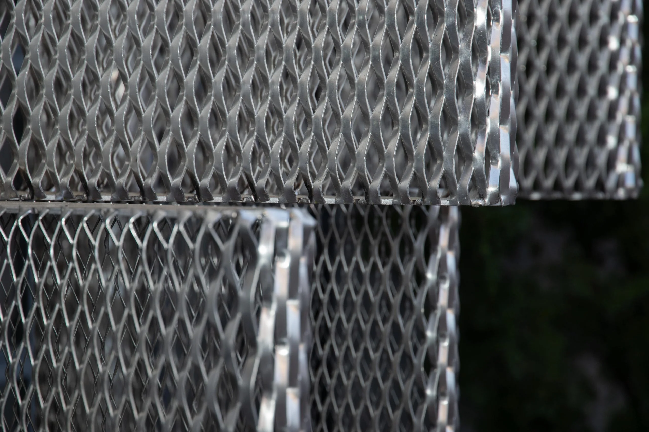 Dettaglio di moduli in lamiera stirata argentata impilati contro il fogliame scuro – Everything Is a Party al Fuorisalone, Milano, Italia, 2025 – progettazione di eventi