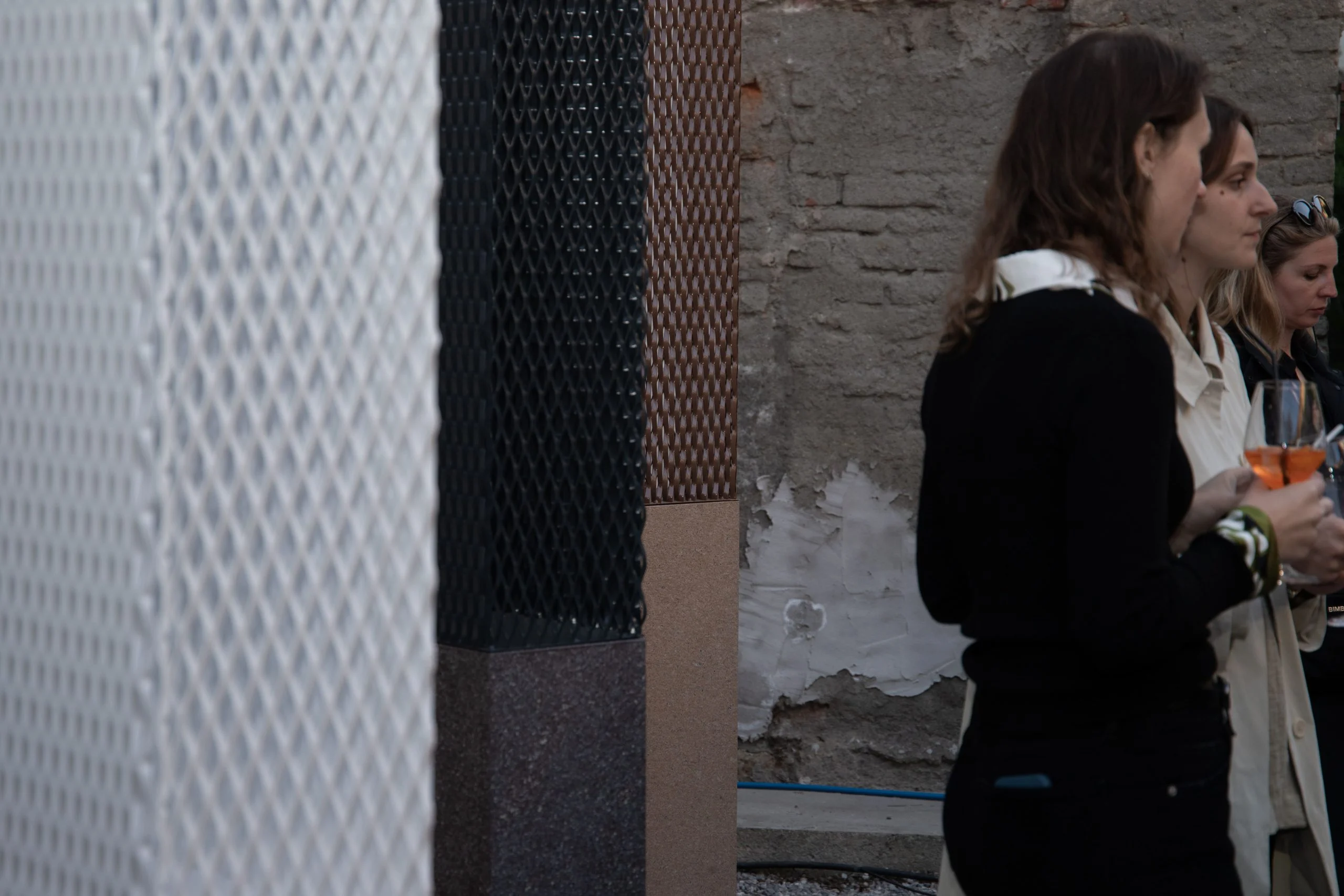 Ospiti con un drink accanto a colonne in rete metallica bianca e nera su basi di pietra – Everything Is a Party al Fuorisalone, Milano, Italia, 2025 – progettazione di eventi