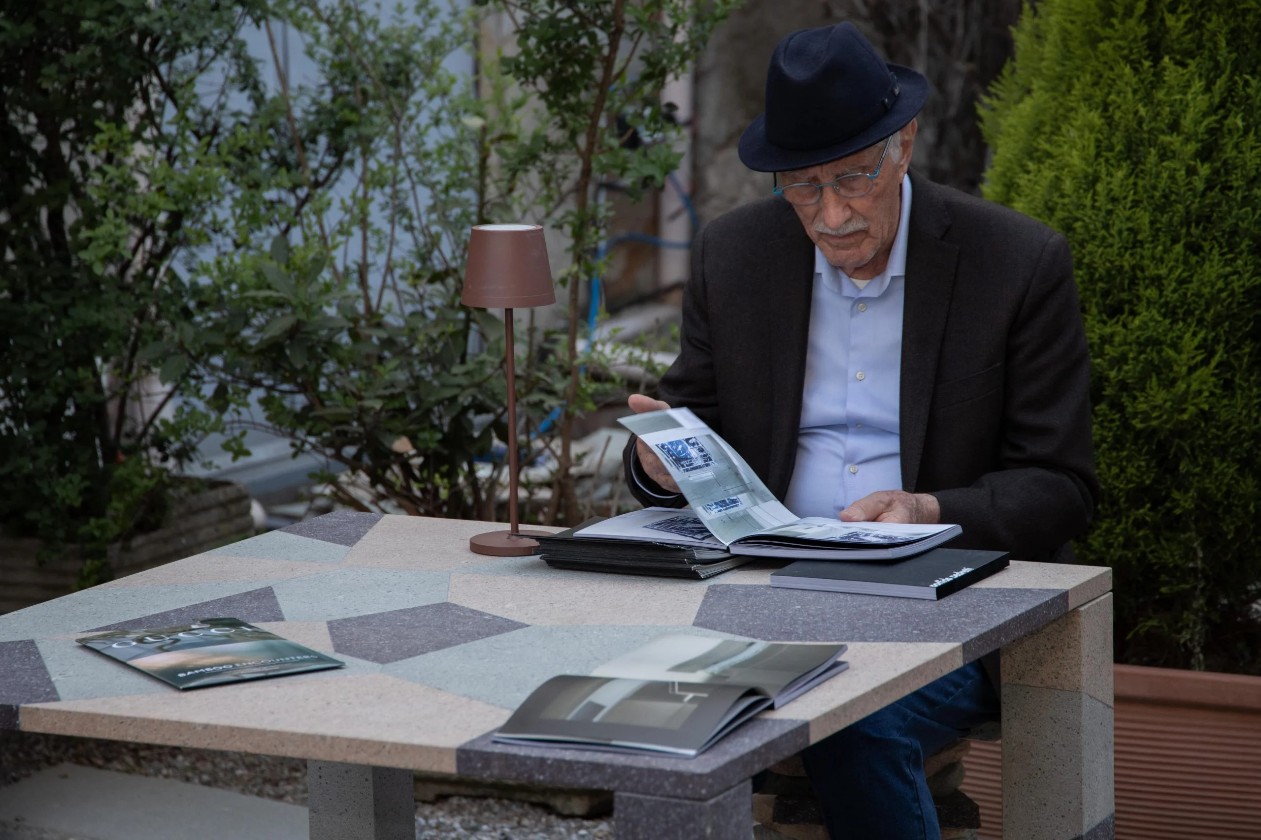 Ospite che legge un catalogo a un tavolo in porfido all'aperto con piano a intarsi geometrici – Everything Is a Party al Fuorisalone, Milano, Italia, 2025 – progettazione di eventi