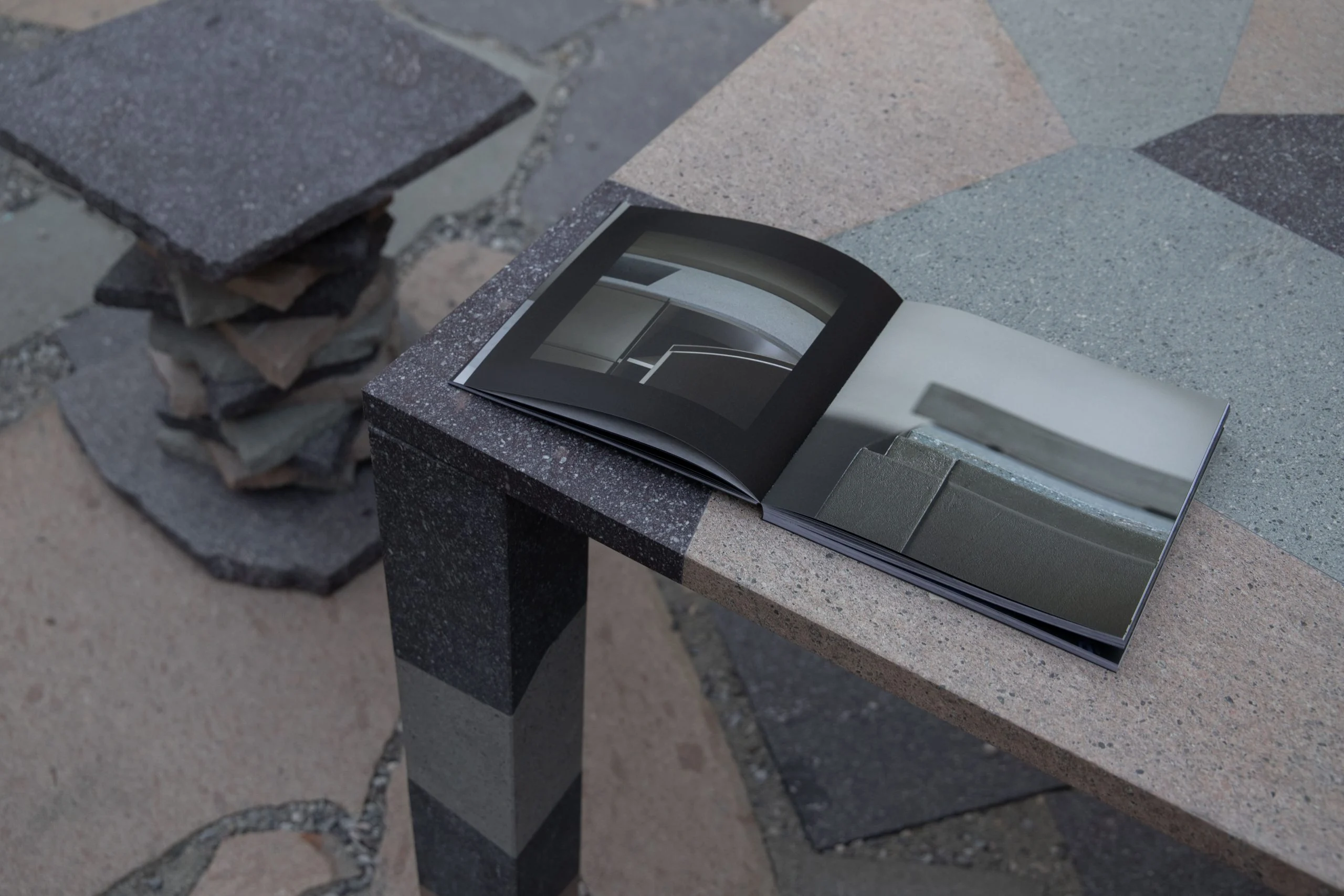 Libro aperto su un tavolo in porfido con piano a intarsi geometrici, dietro uno sgabello di pietre impilate – Everything Is a Party al Fuorisalone, Milano, Italia, 2025 – progettazione di eventi
