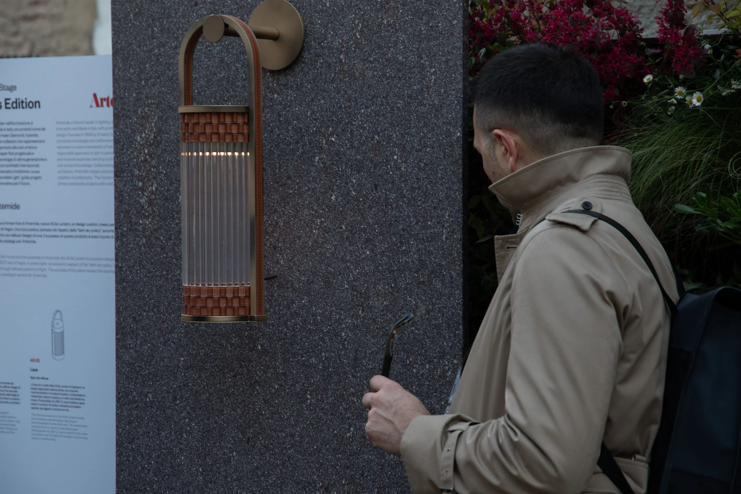 Ospite che guarda un'applique in bronzo e vetro montata su un pannello di pietra scura – Everything Is a Party al Fuorisalone, Milano, Italia, 2025 – progettazione di eventi