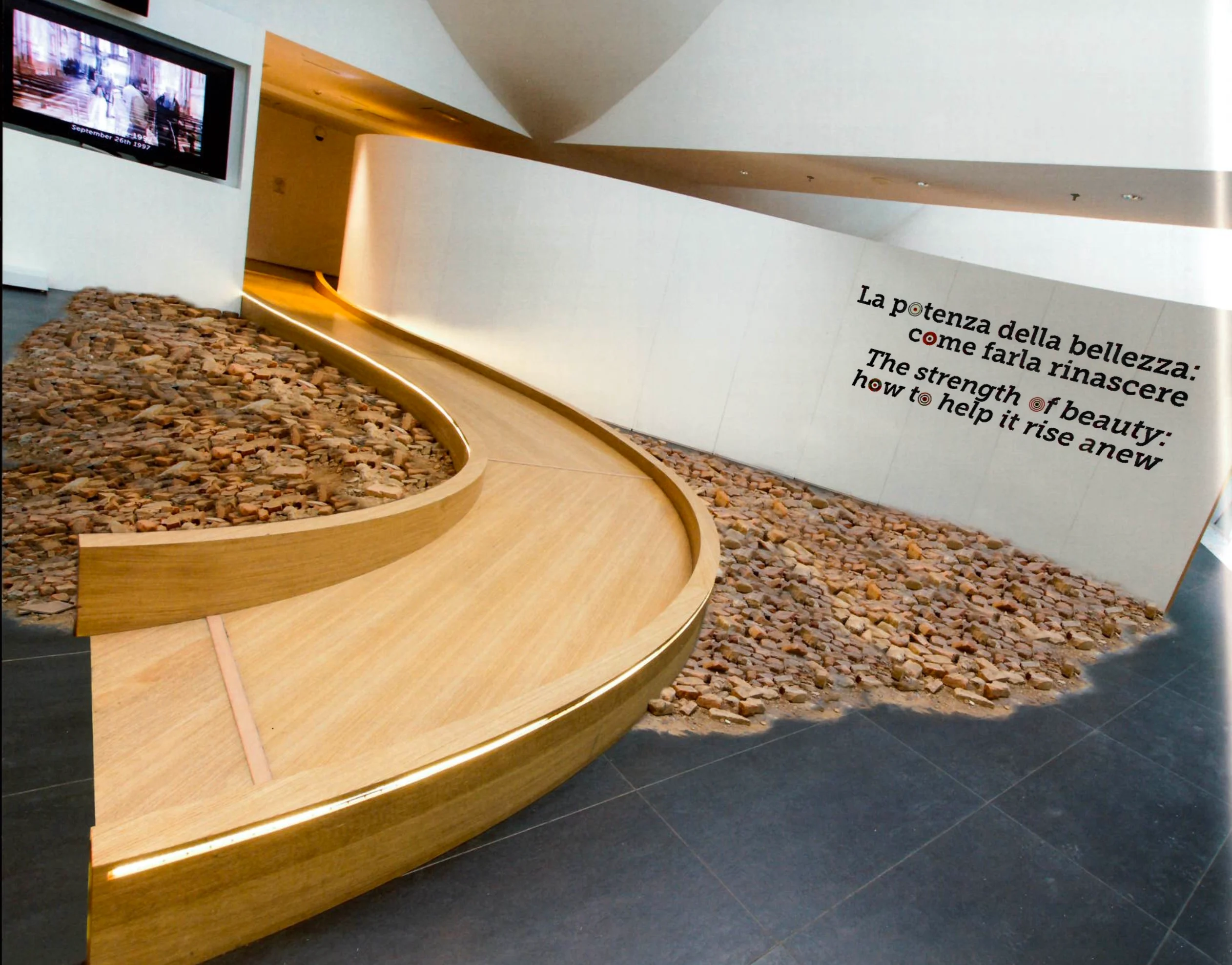 Passerella curva in legno su un letto di macerie, con il testo bilingue The strength of beauty sulla parete – Padiglione Italia all'Expo 2015, Milano, Italia – allestimento espositivo