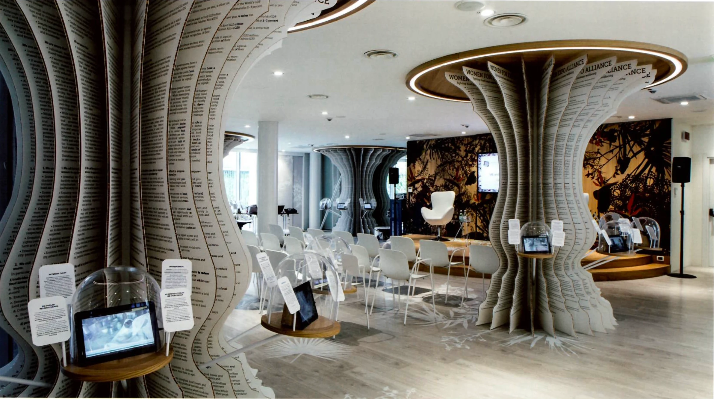 Spazio espositivo con colonne ad albero in strati di carta, sedie bianche e tablet sotto campane di vetro – Padiglione Italia all'Expo 2015, Milano, Italia – allestimento espositivo