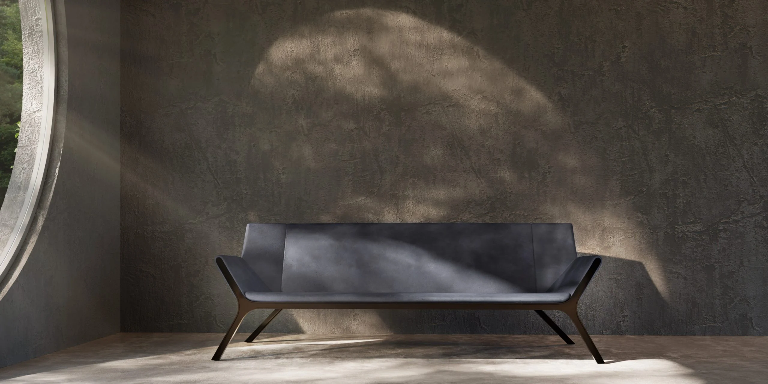 Divano imbottito scuro con gambe metalliche inclinate in una stanza in cemento grezzo illuminata da una finestra rotonda – Collezione FRAME Tonino Lamborghini, Milano, Italia, 2025 – design di prodotto
