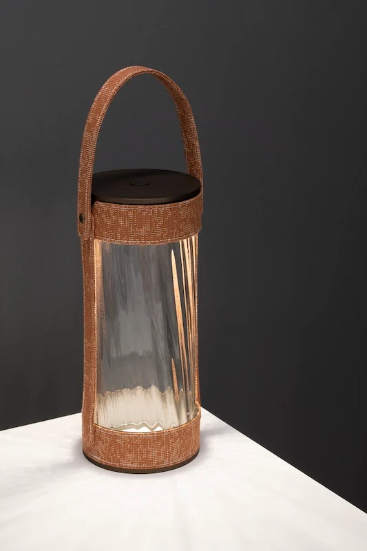 Lanterna con cinghia intrecciata color terracotta e vetro rigato su un tavolo bianco, sfondo scuro – Lanterna AlUla per Artemide, Milano, Italia, 2025 – lighting design