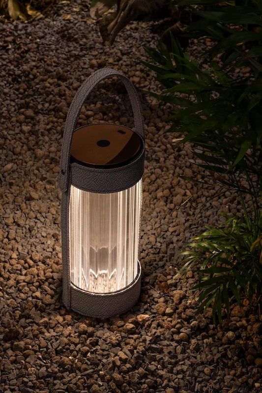 Lanterna con cinghia grigia accesa sulla ghiaia tra le piante di notte – Lanterna AlUla per Artemide, Milano, Italia, 2025 – lighting design