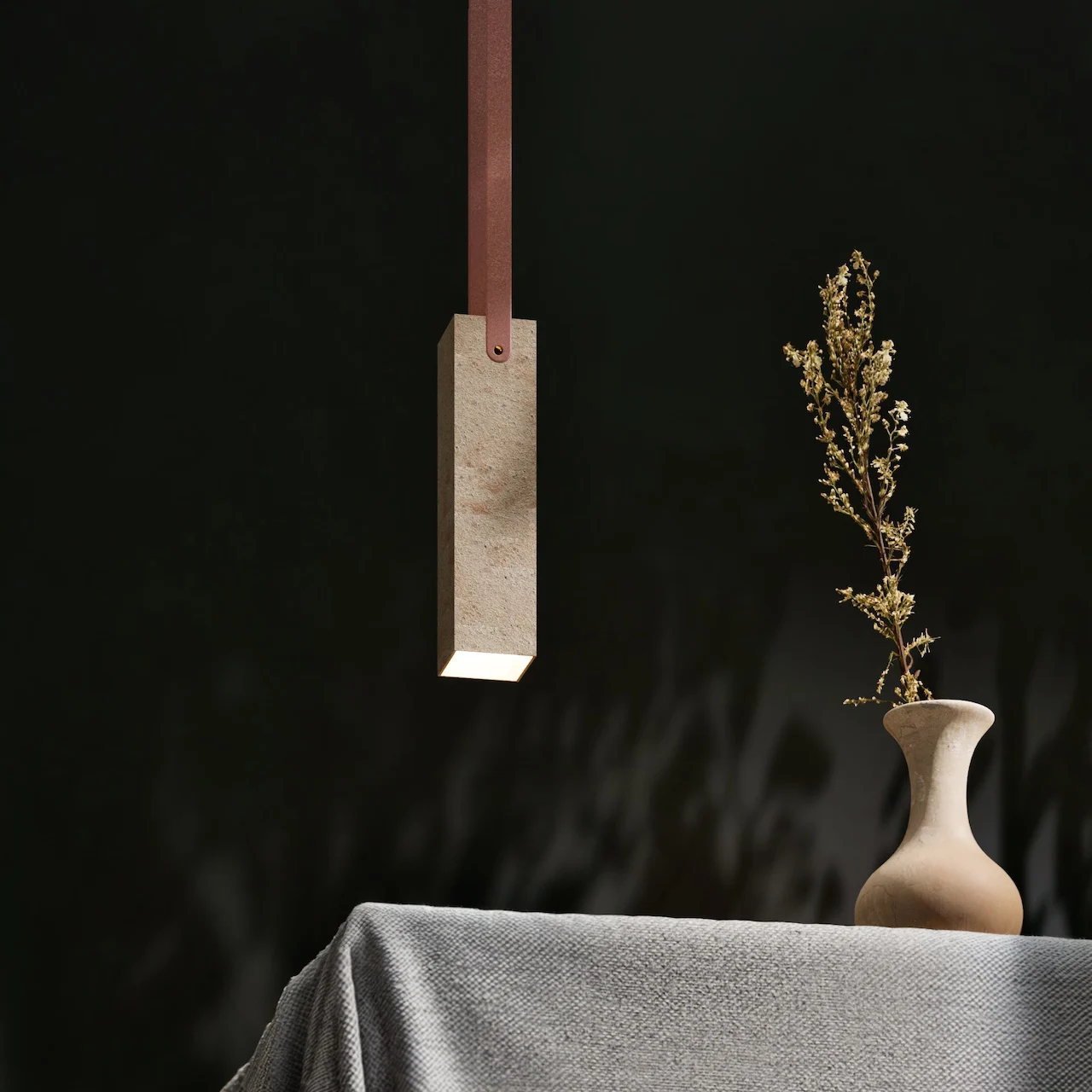 Lampada a sospensione rettangolare in pietra con cinghia di pelle sopra un tavolo con un vaso di fiori secchi – Arredi in porfido Porfido Pedretti, Milano, Italia, 2025 – design di prodotto