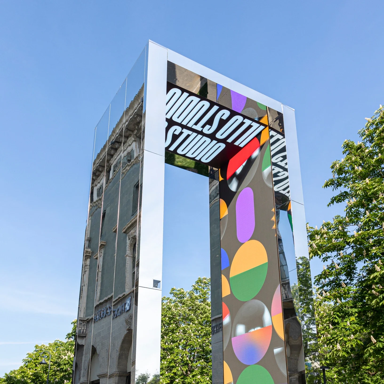 Vista dal basso del portale a specchio con grafiche LED colorate e la scritta Studio contro il cielo blu – THE GATE 2023, Bergamo e Brescia, Italia – progettazione di installazioni