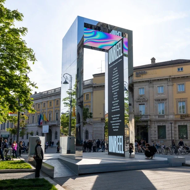 Portale a specchio con architrave LED iridescente e un alto schermo UNREEL, persone raccolte intorno – THE GATE 2023, Bergamo e Brescia, Italia – progettazione di installazioni