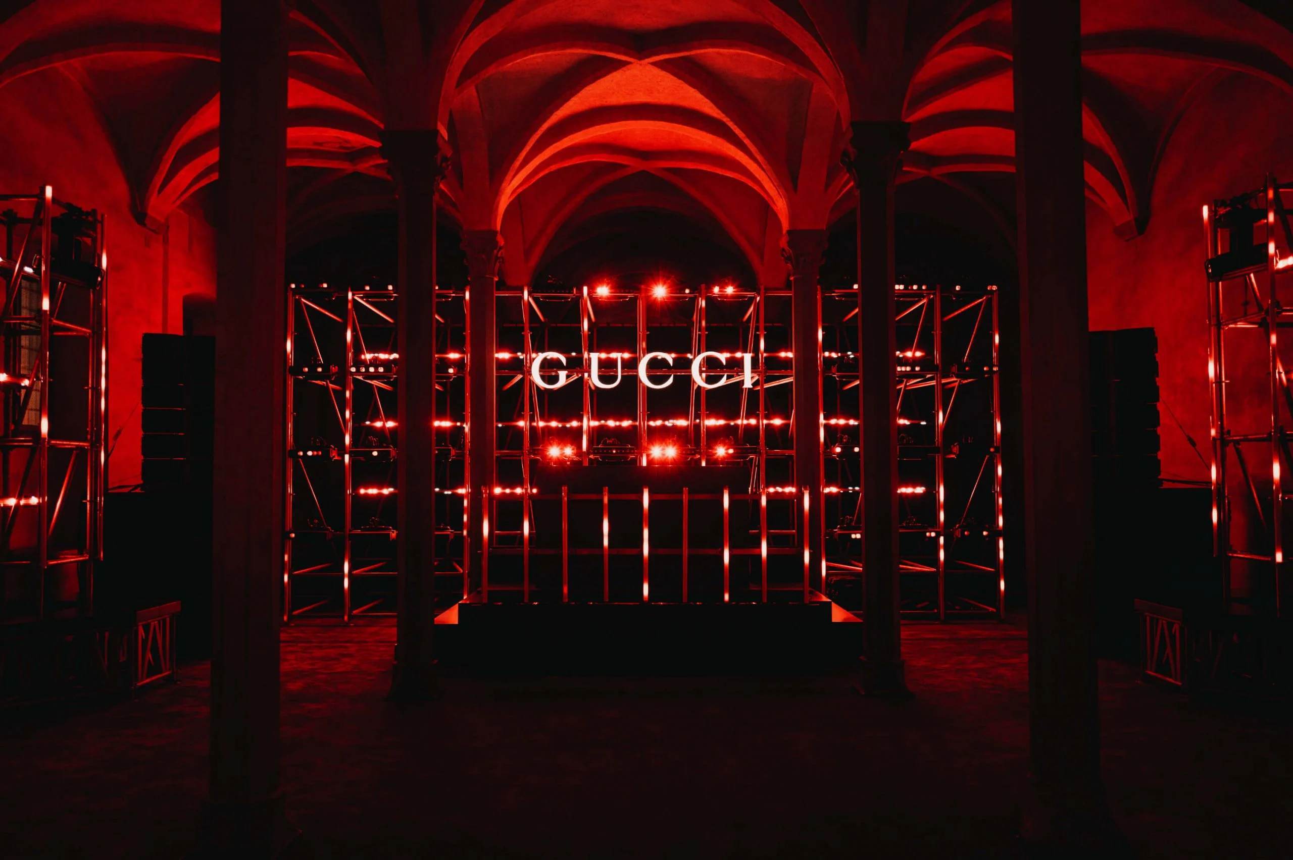 Sala a volte inondata di rosso con torri di impalcature e un'insegna GUCCI al centro – Gucci Cruise 2026 Afterparty, Firenze, Italia, 2025 – progettazione di eventi