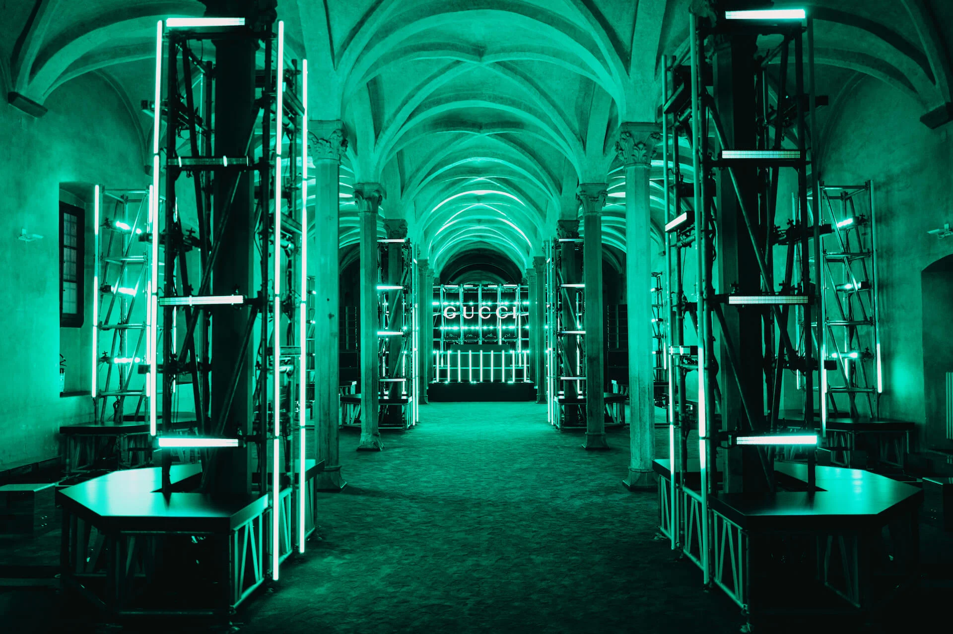 Sala a volte immersa nella luce verde, torri di impalcature illuminate che conducono a un'insegna GUCCI – Gucci Cruise 2026 Afterparty, Firenze, Italia, 2025 – progettazione di eventi