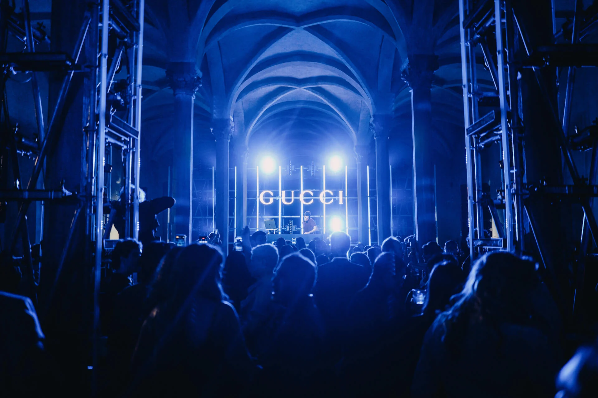 Folla in luce blu davanti a un'insegna GUCCI illuminata e riflettori abbaglianti, impalcature ai lati – Gucci Cruise 2026 Afterparty, Firenze, Italia, 2025 – progettazione di eventi
