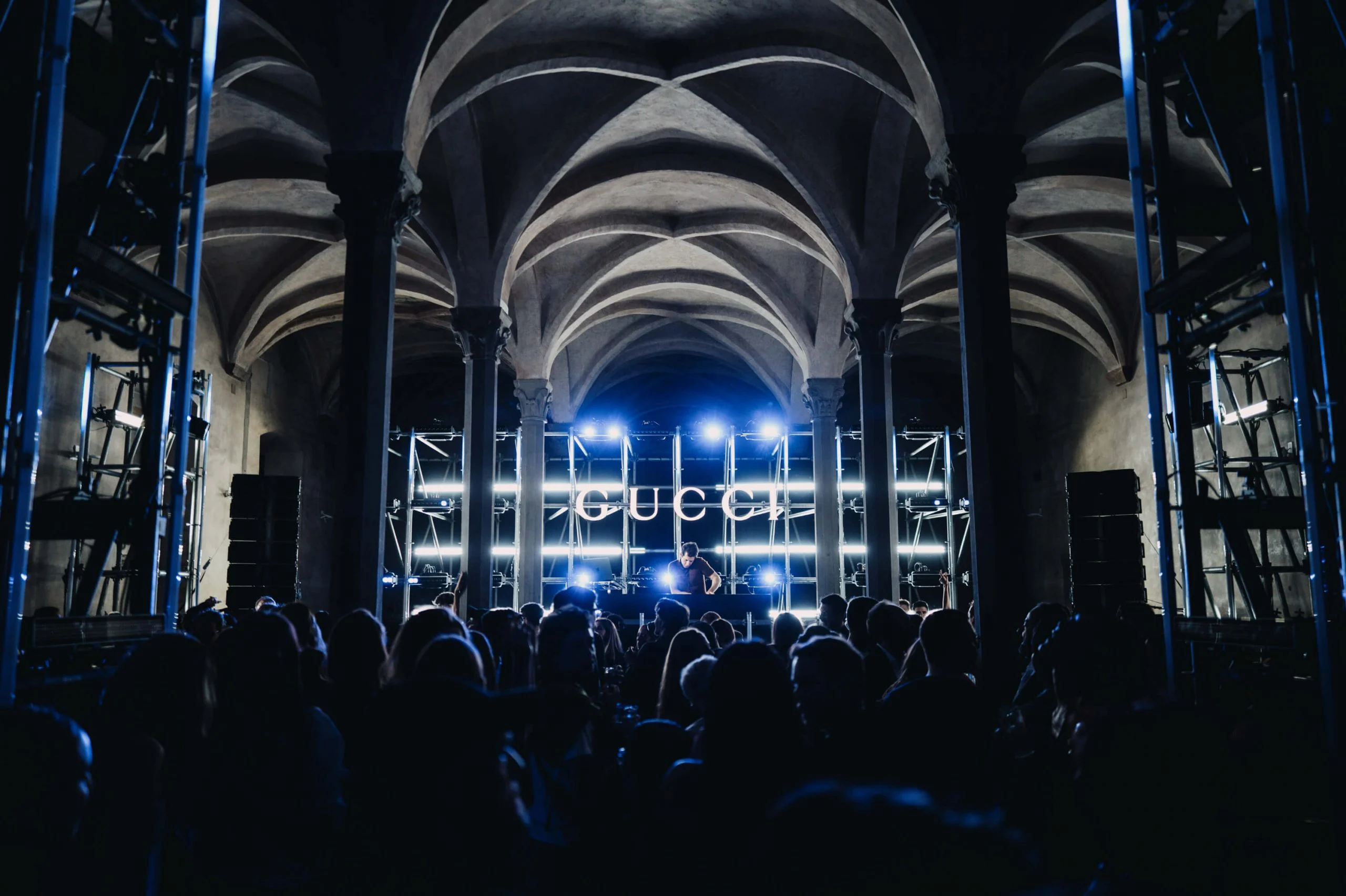 Folla sotto il soffitto a volte davanti a una consolle DJ con un'insegna GUCCI e luci bianche – Gucci Cruise 2026 Afterparty, Firenze, Italia, 2025 – progettazione di eventi