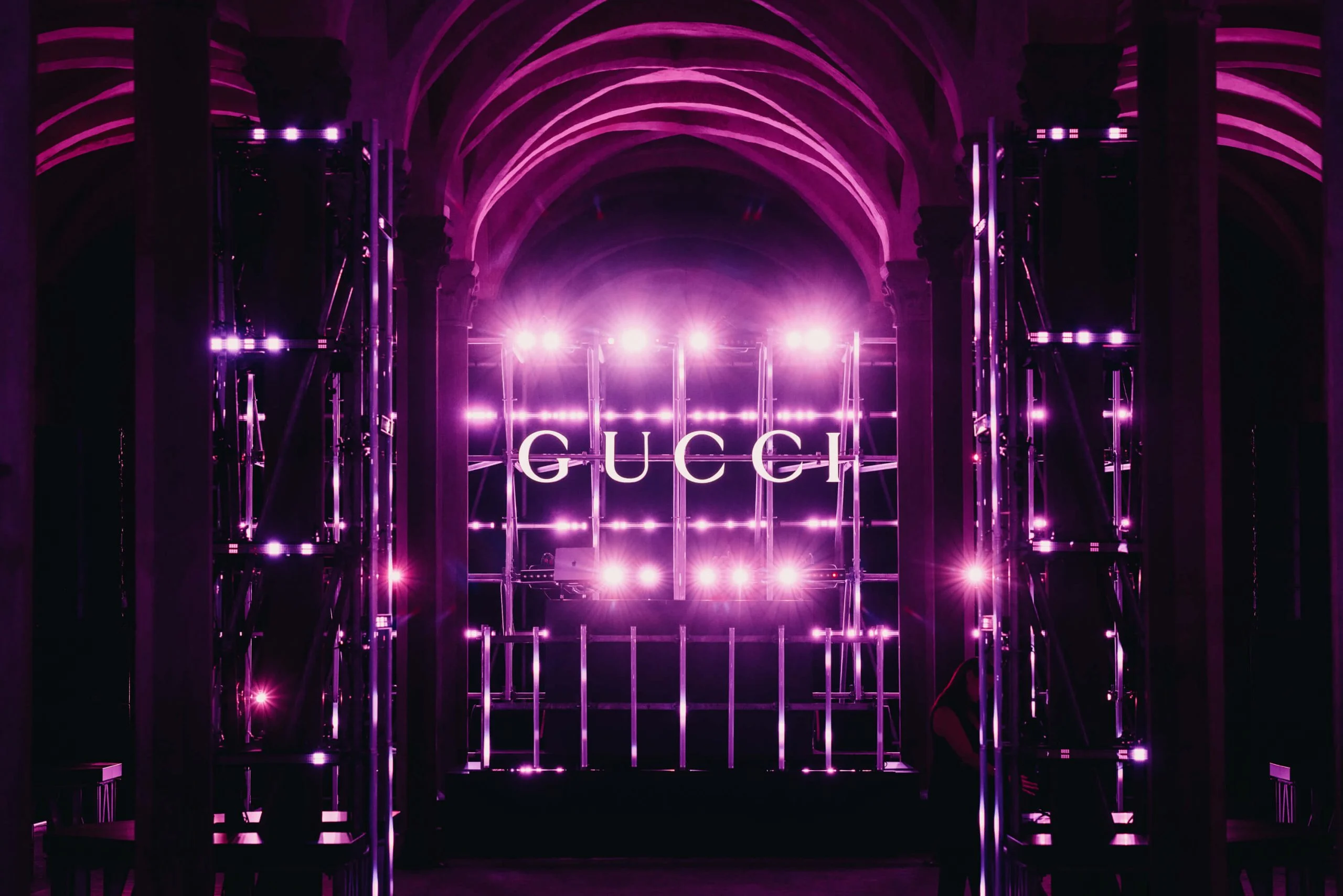 Palco di impalcature con un'insegna GUCCI accesa in luce rosa e viola sotto le volte – Gucci Cruise 2026 Afterparty, Firenze, Italia, 2025 – progettazione di eventi