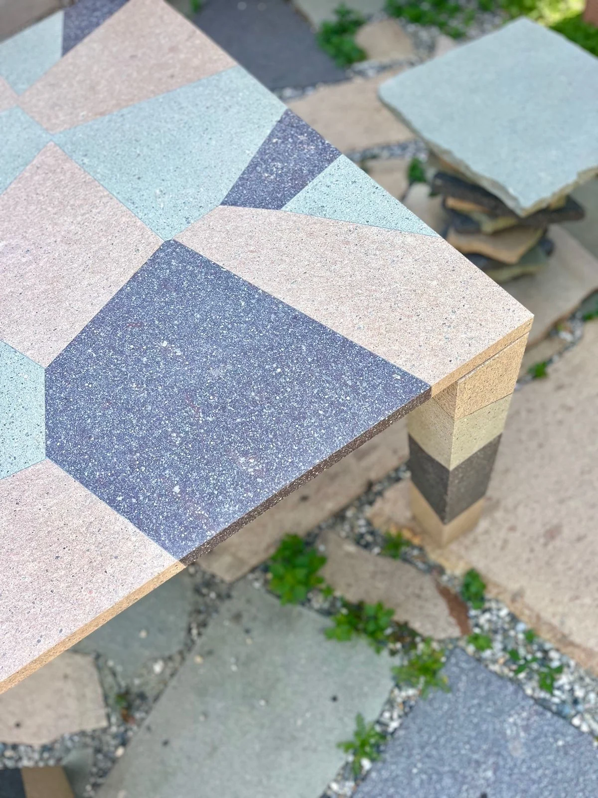Angolo di un tavolo con piano intarsiato in porfido rosa, verde e scuro e una gamba a strisce – Collezione Frammenti per Porfido Pedretti, Milano, Italia, 2025 – design di prodotto